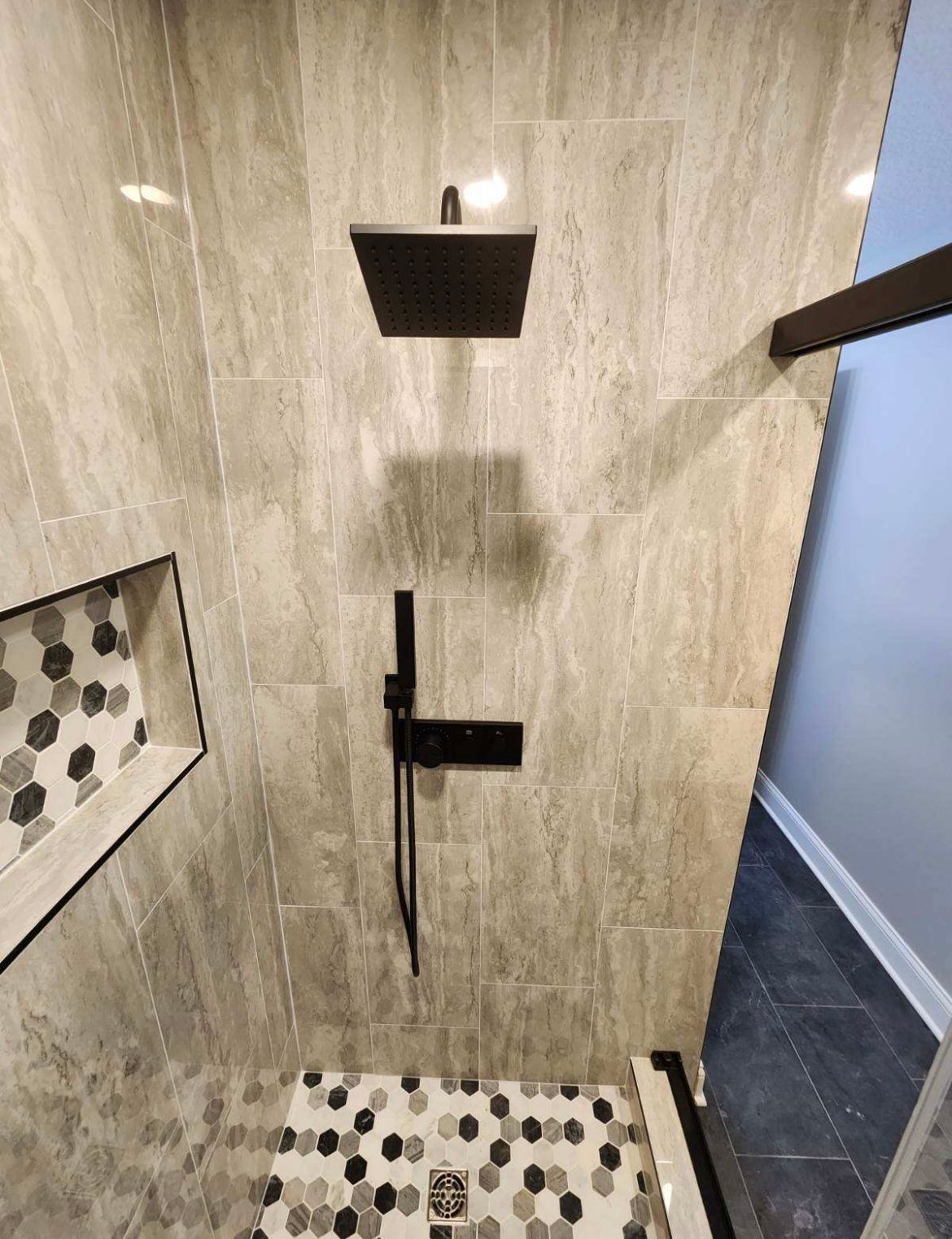 A bathroom with a square shower head and a tiled floor.