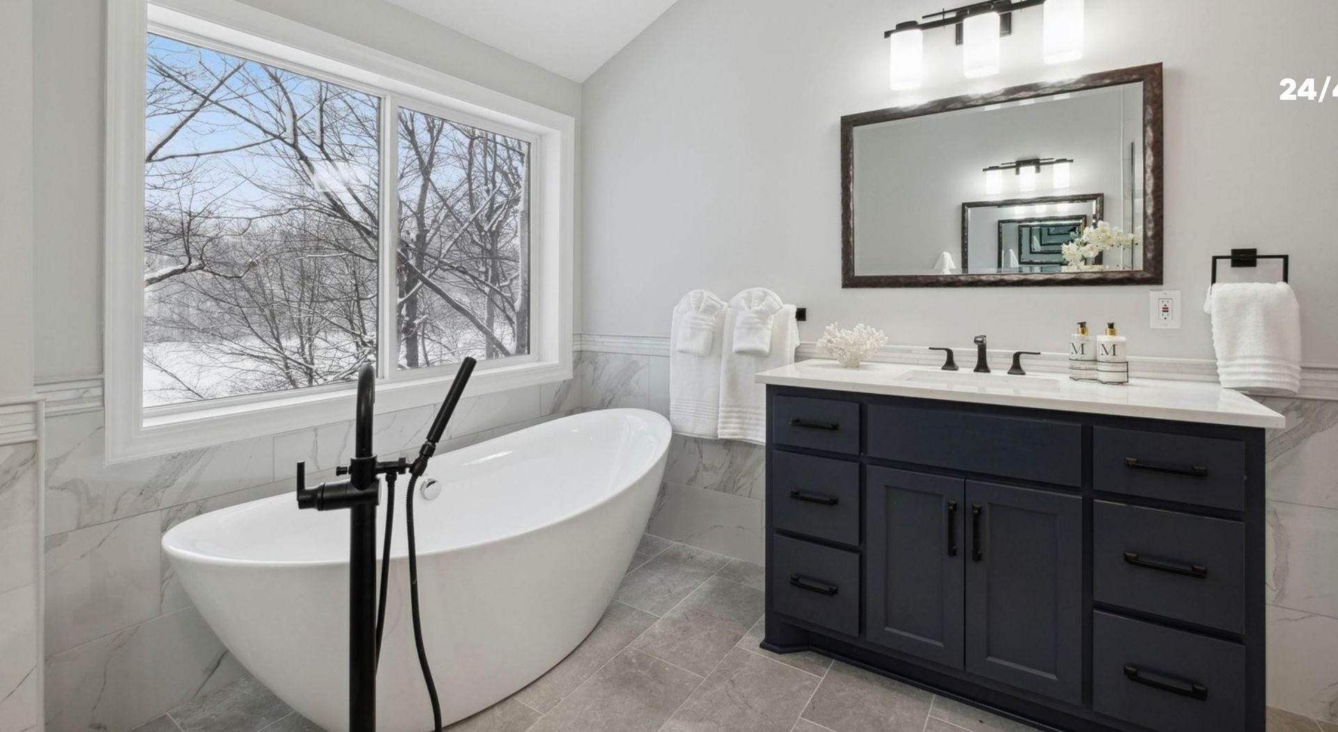 A bathroom with a tub , sink , mirror and window.