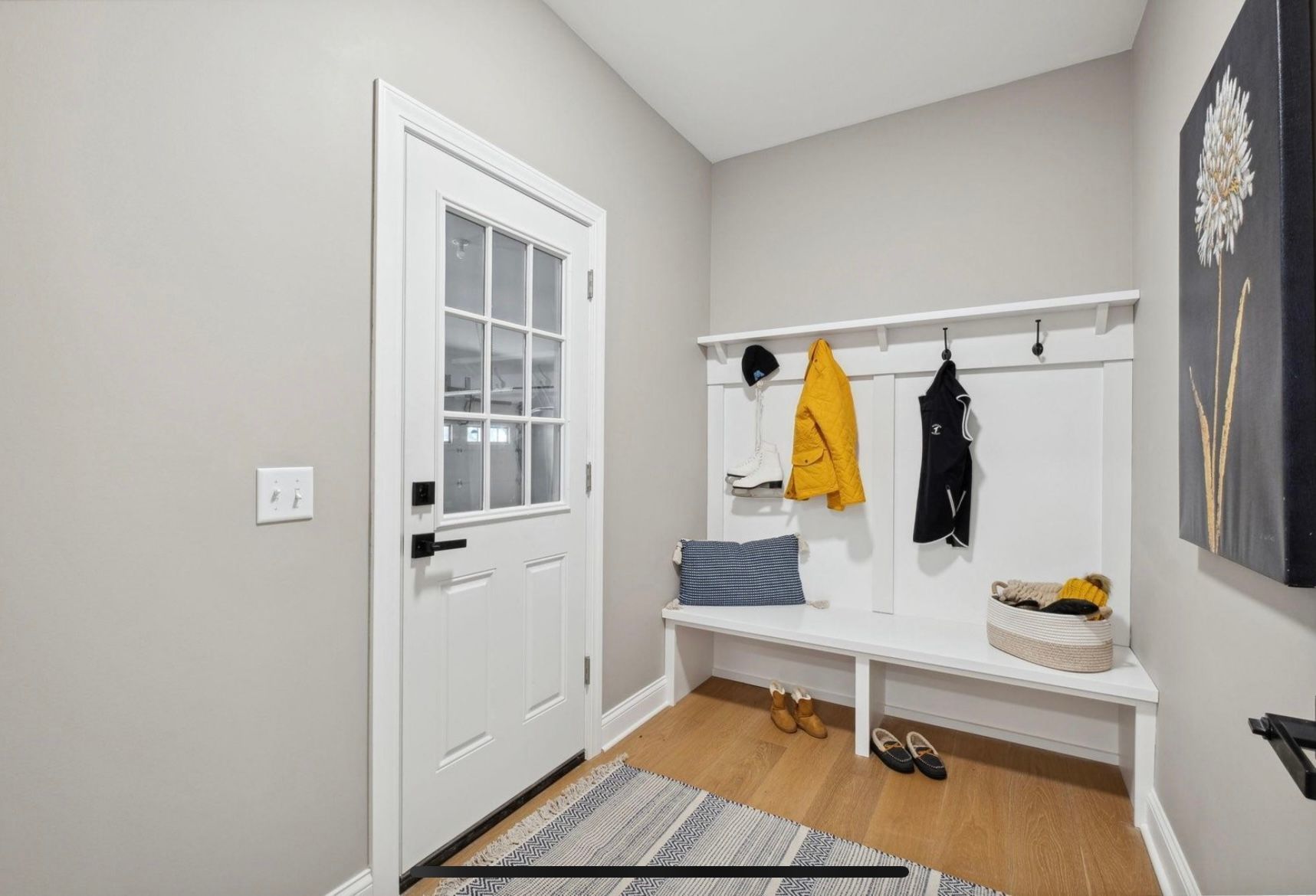 There is a bench in the mud room with clothes hanging on the wall.