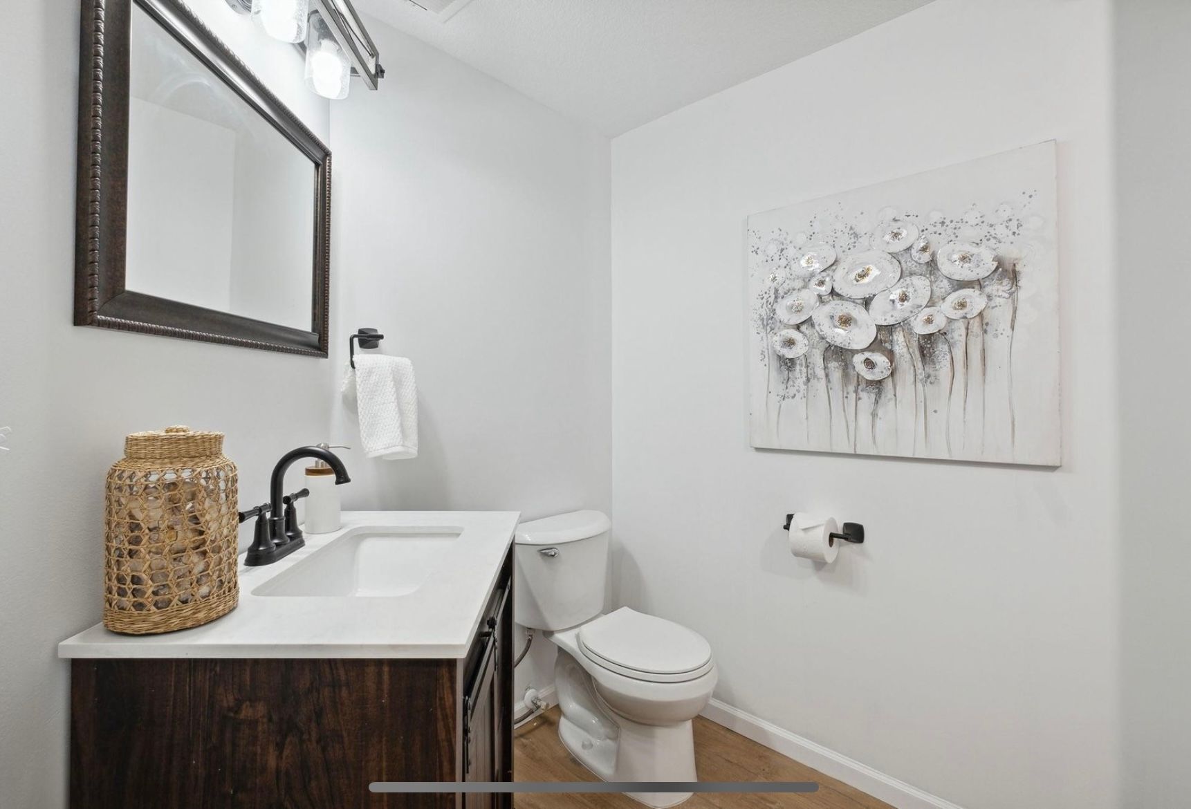 A bathroom with a sink , toilet , mirror and painting on the wall.