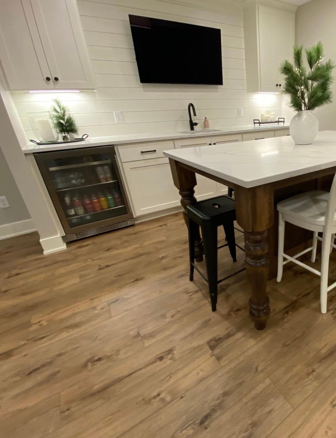 A kitchen with a table , chairs , a refrigerator and a flat screen tv.