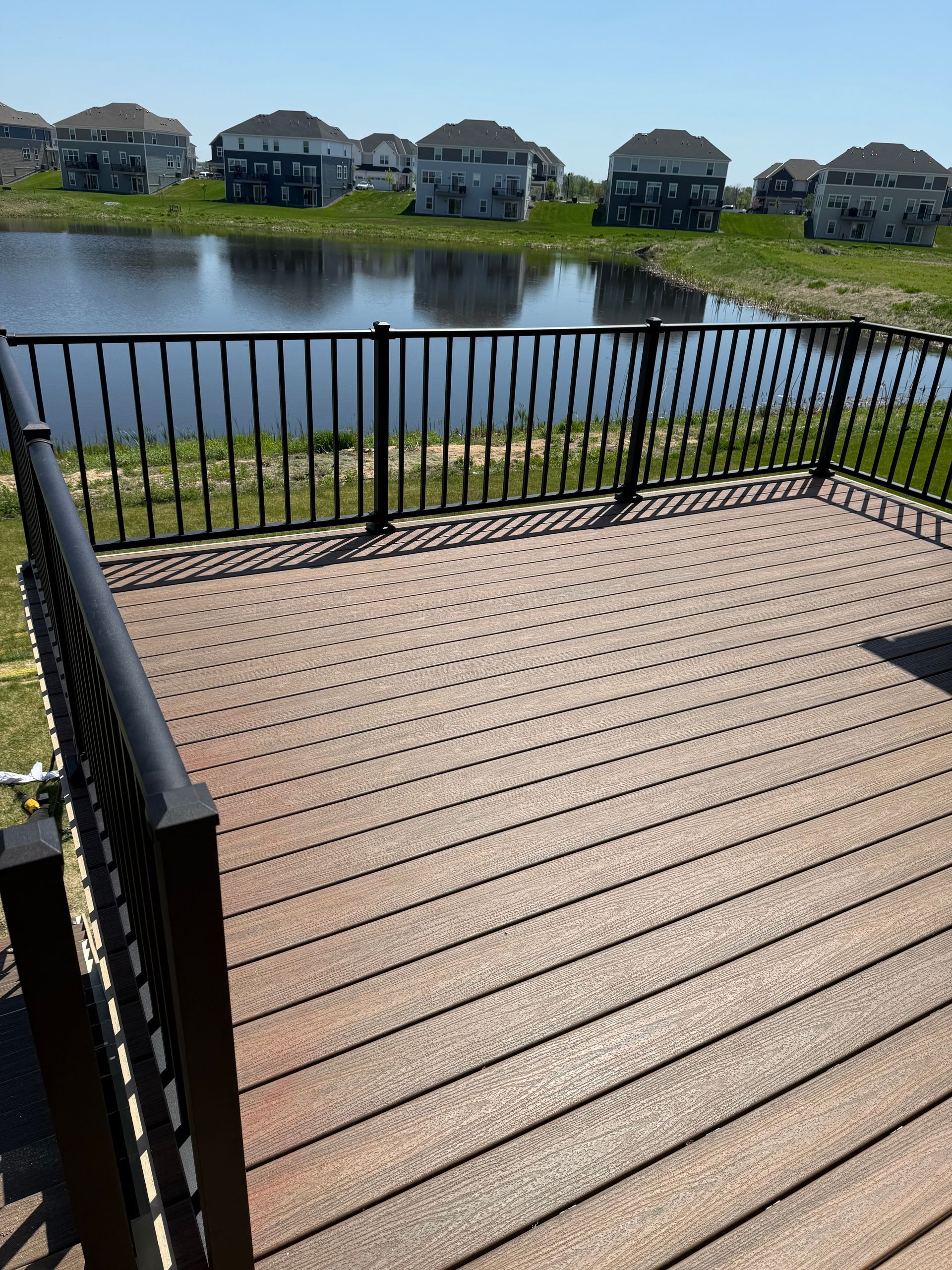 A deck with a railing overlooking a lake with houses in the background.