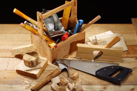 Wooden toolbox filled with woodworking tools on a wooden surface with wood pieces and a saw.