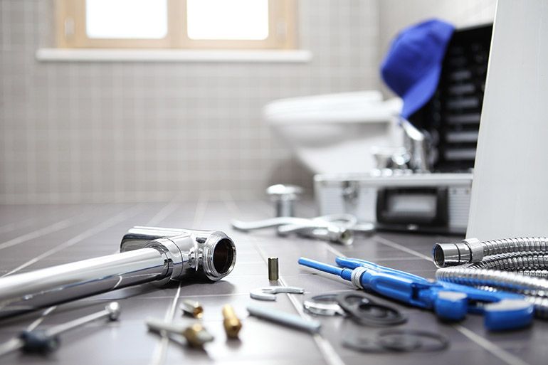 Plumbing tools scattered on a bathroom floor, near a toilet and open toolbox.