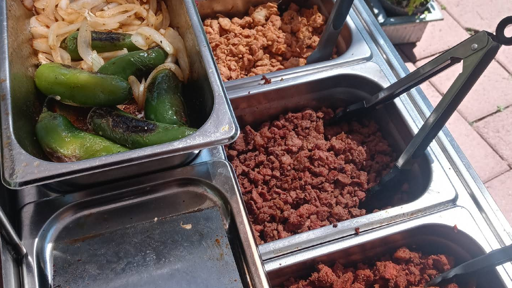 A food cart with various fillings: grilled peppers and onions, and several meats, ready to serve.