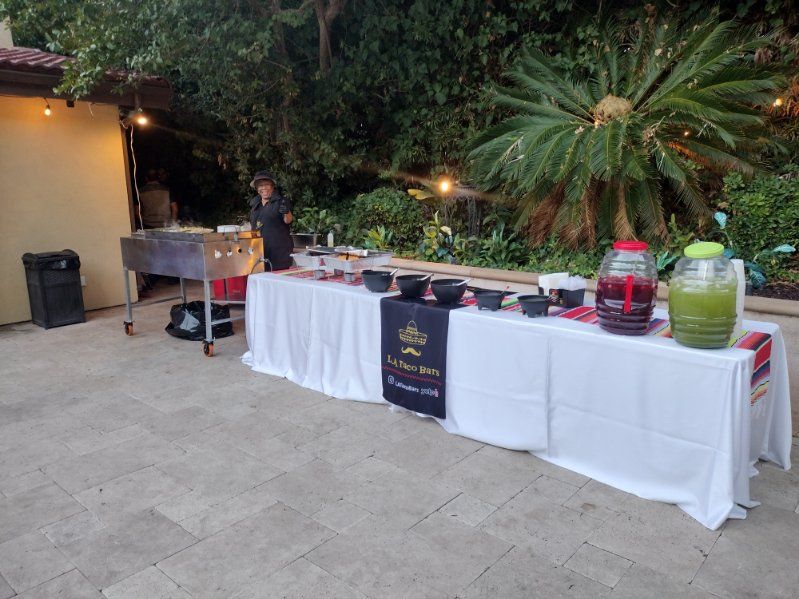 Outdoor food station with a cook, buffet table, and grilling station; drinks and food served.
