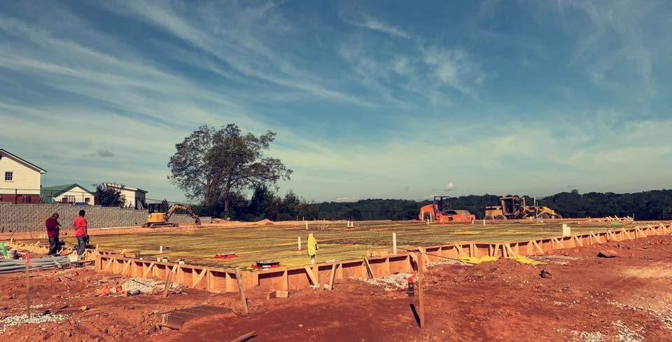 Construction site with wooden forms and workers on red dirt under a blue sky