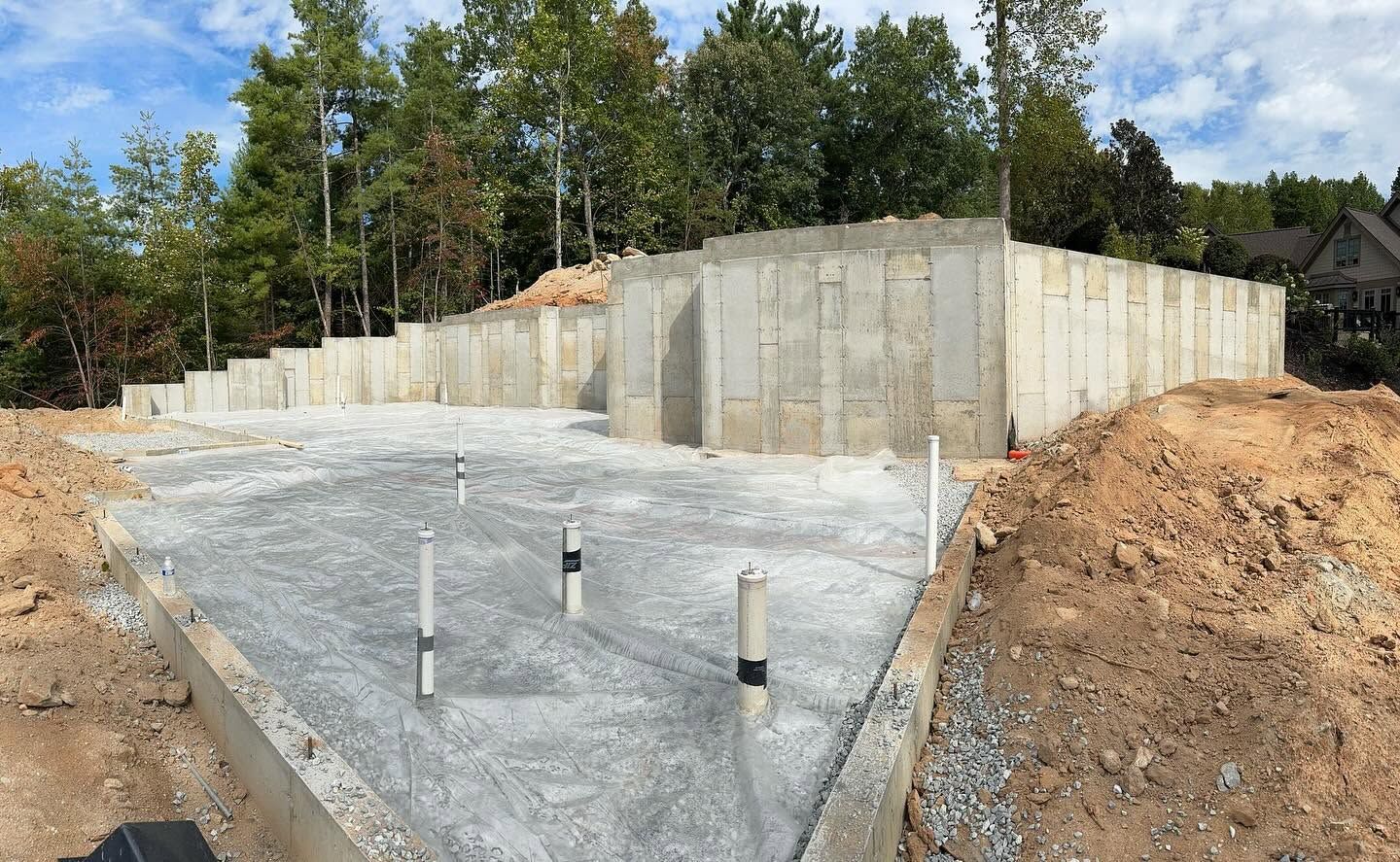 Concrete foundation with retaining walls and exposed pipes on a construction site surrounded by trees