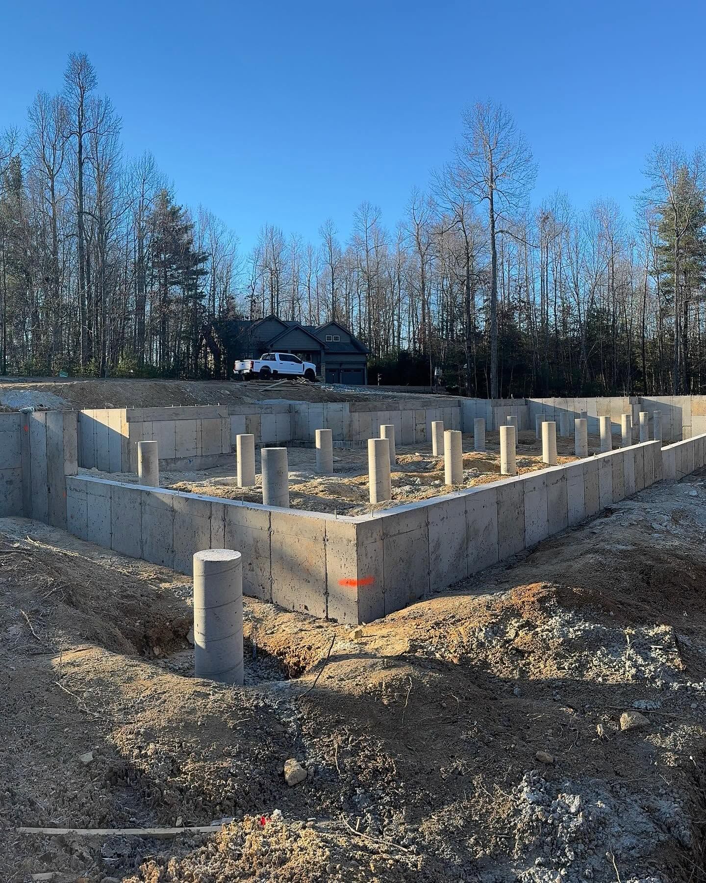 Concrete foundation walls under construction in a wooded area with blue sky