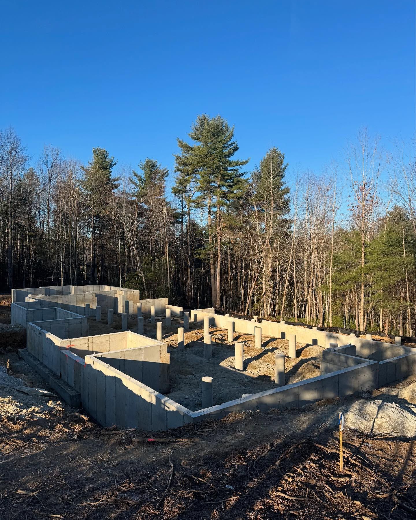 Foundation under construction in a wooded area, with concrete walls and a clear blue sky.