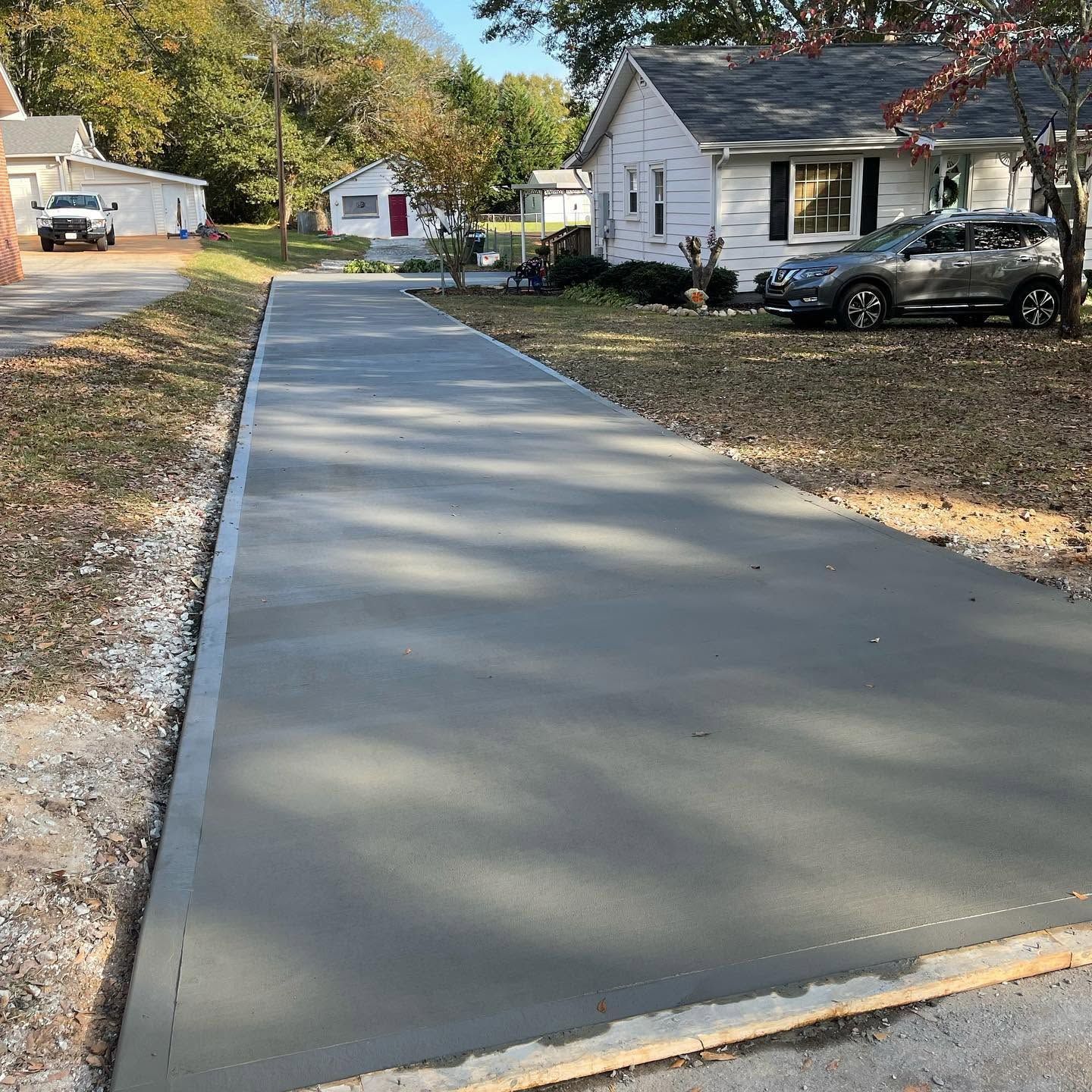 Fresh concrete driveway beside a white house in a quiet suburban neighborhood, with fall leaves scattered nearby