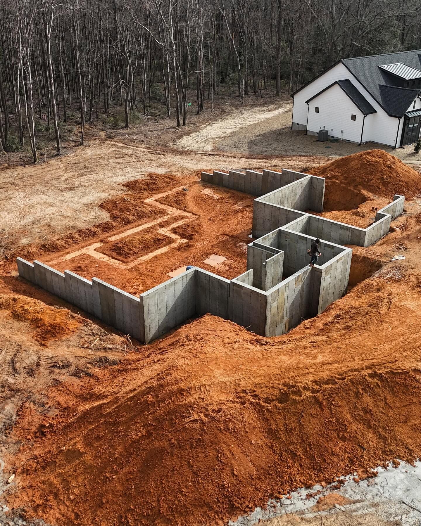 House foundation under construction on a muddy lot beside a wooded area