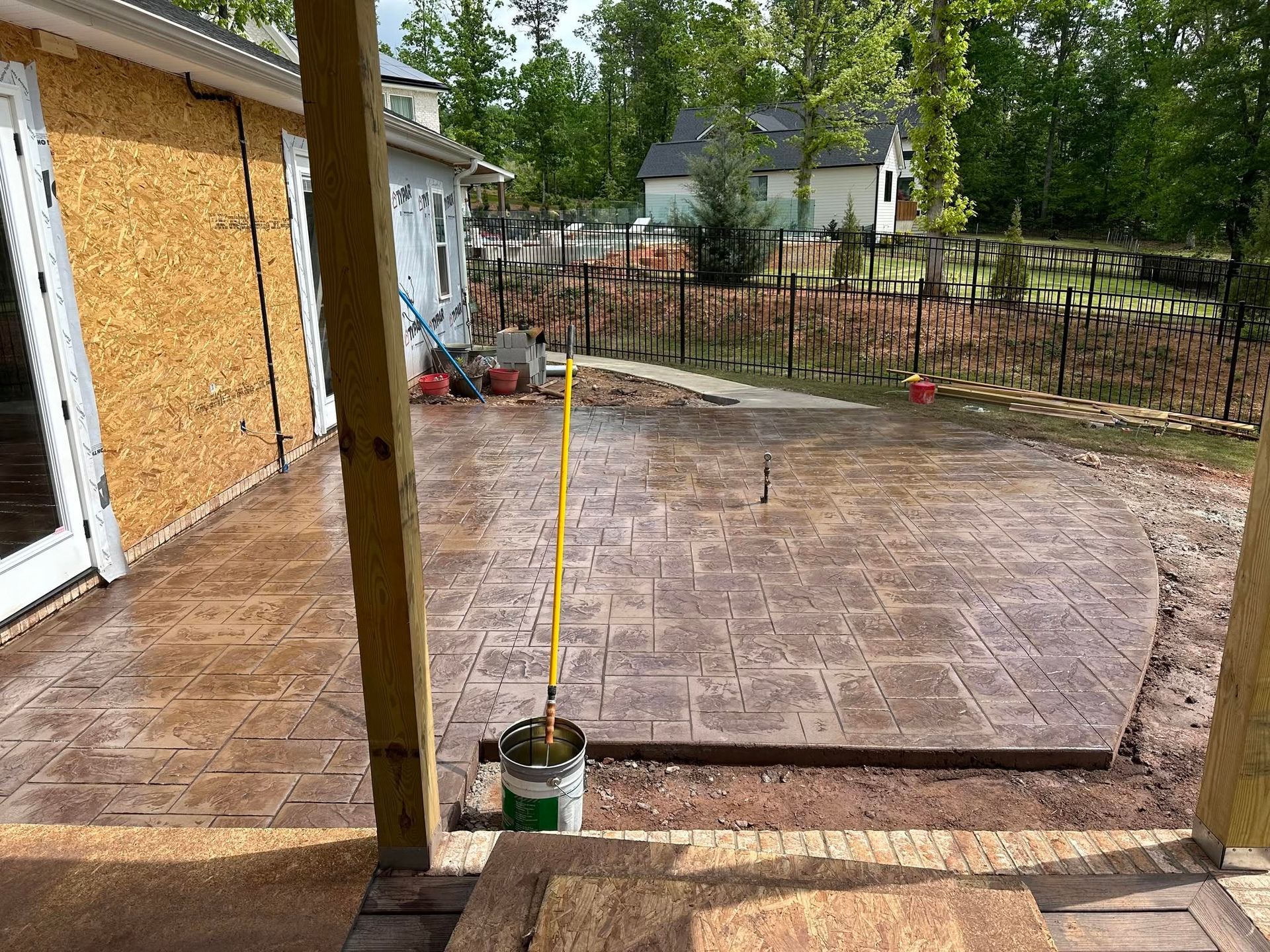 Backyard patio with stamped concrete, wooden posts, and a fenced yard under construction