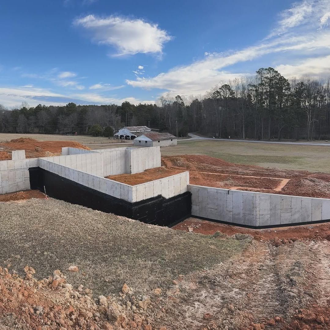 Construction site with concrete foundation blocks and a dirt lot under a cloudy blue sky