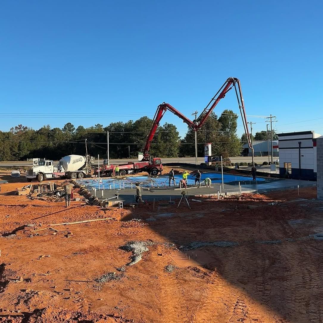 Construction site with red concrete pumps, workers, and a large blue slab under a clear sky