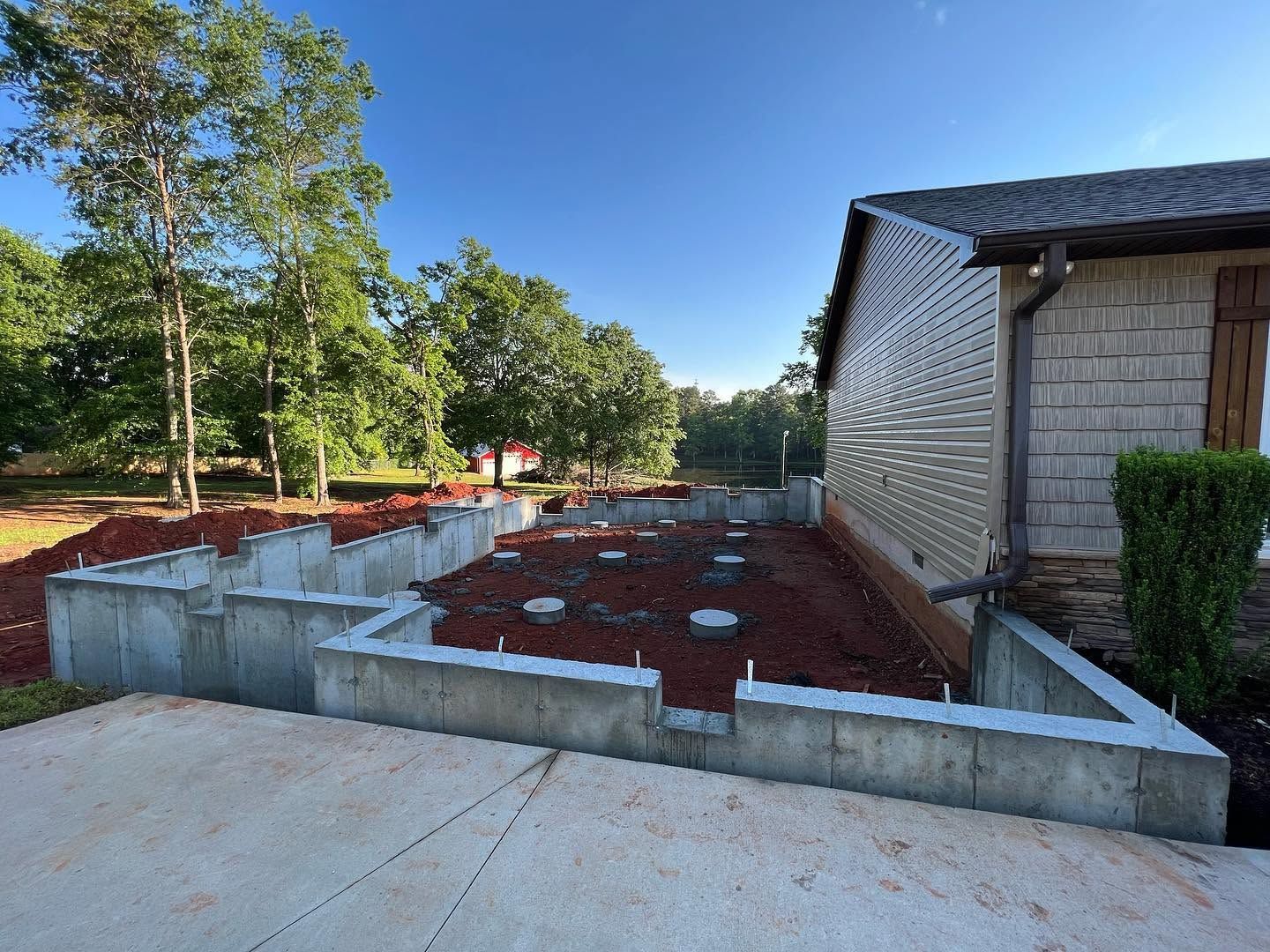 New concrete foundation and red clay-filled beds beside a house in a sunny yard