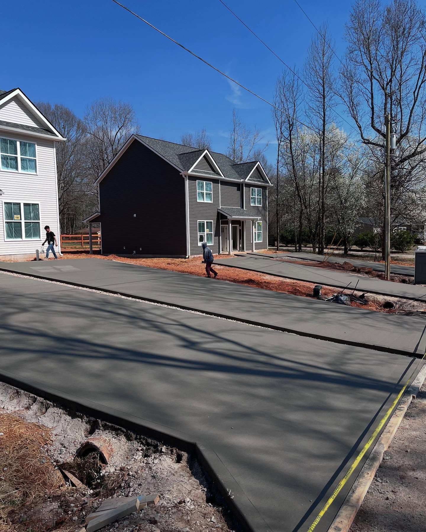 Freshly poured concrete driveway beside houses and leafless trees on a sunny day