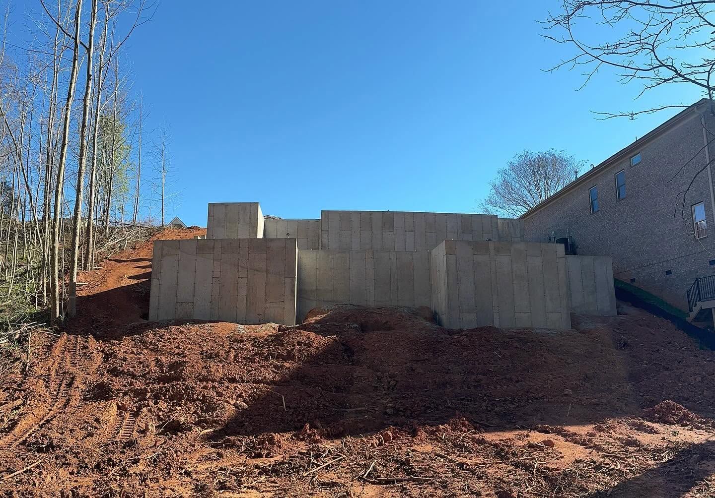 Retaining wall of concrete blocks on a bare dirt slope under a clear blue sky