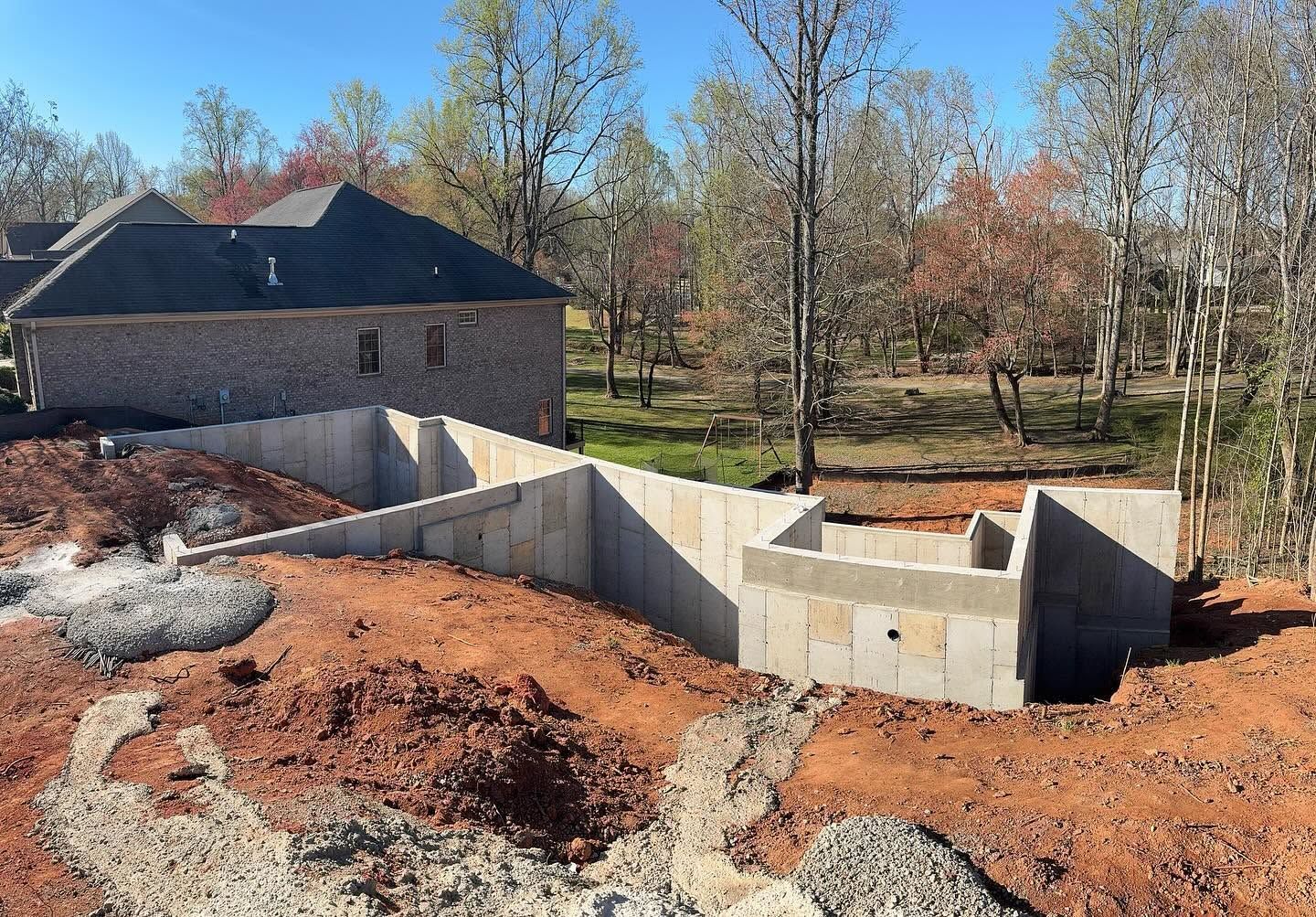 Concrete foundation walls at a construction site beside a house and trees in autumn.