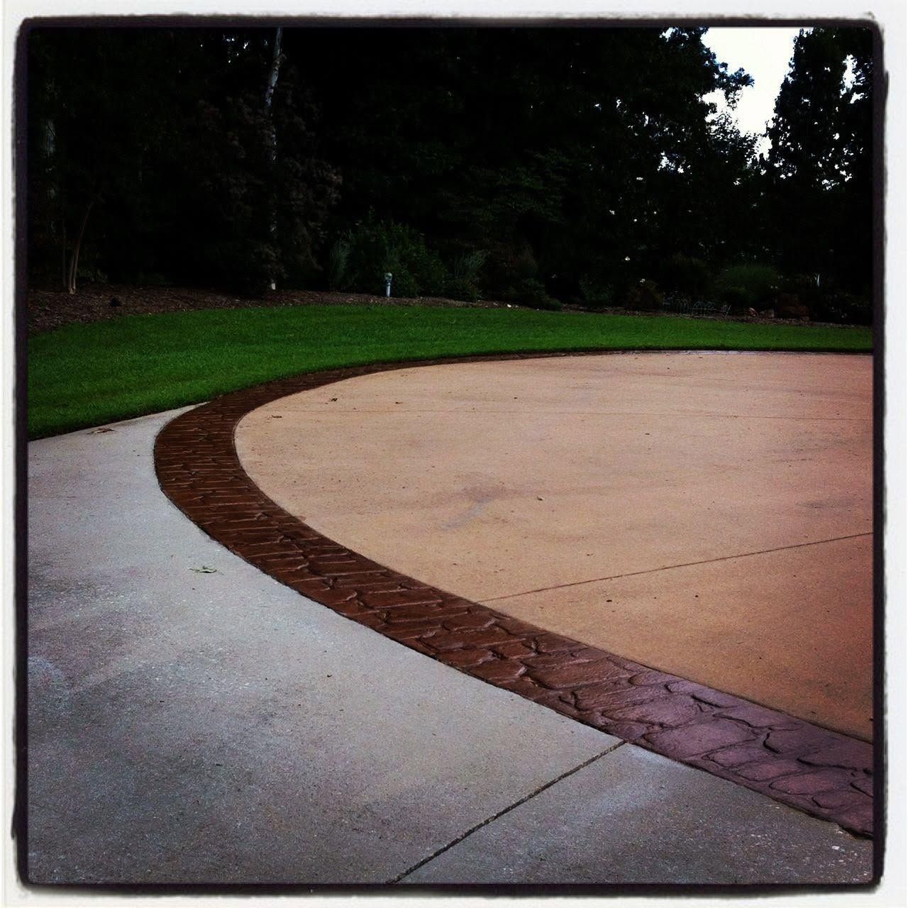 Curved brick border between a concrete path and sandy court in a park, with grass and trees beyond