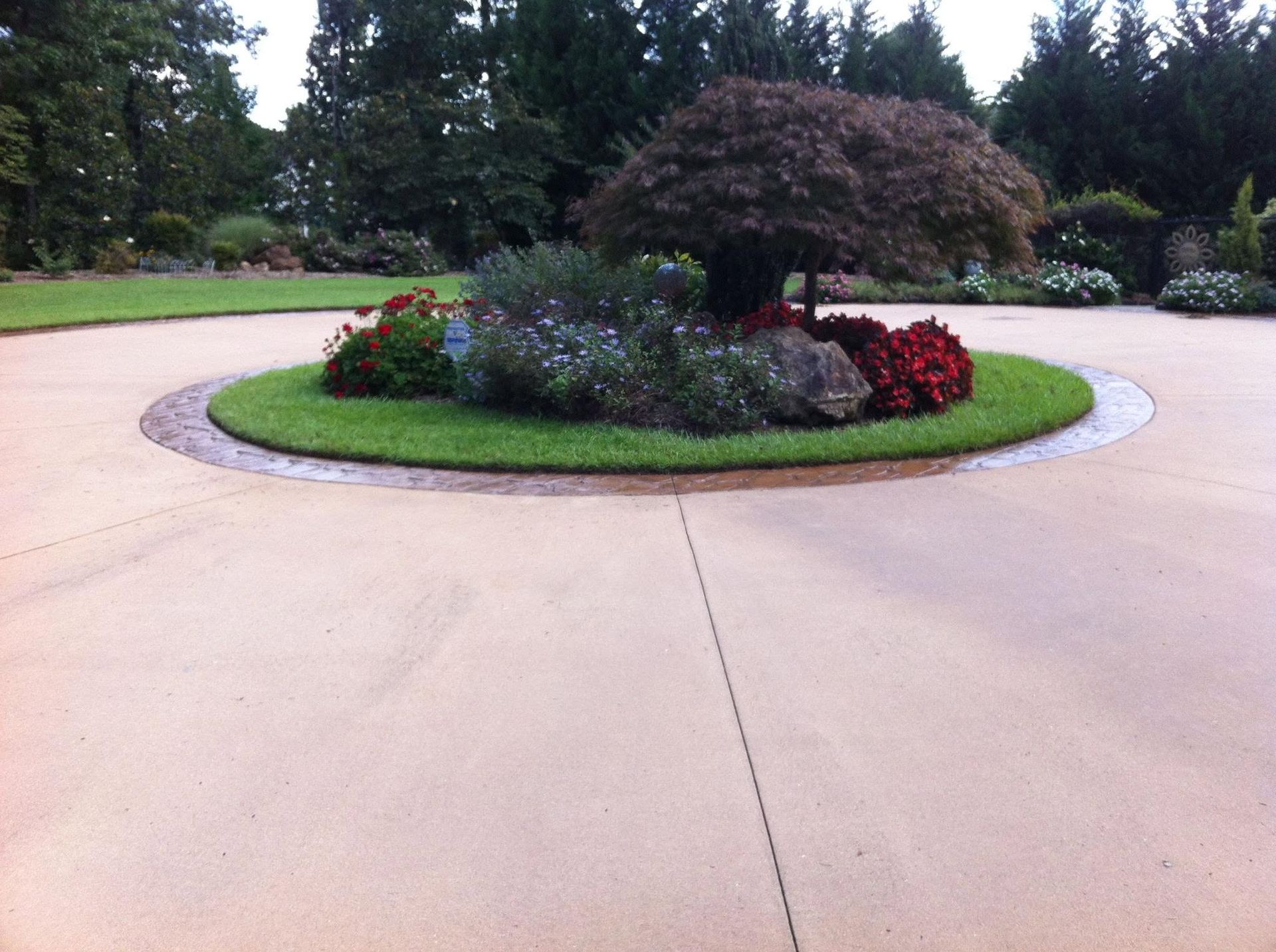 Circular driveway around a landscaped island with flowers and a tree