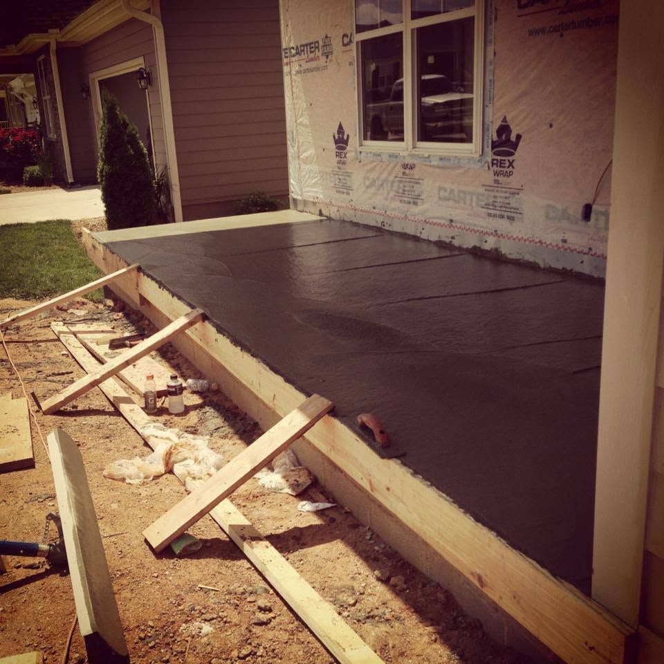 Concrete porch slab under construction beside a house, with wooden forms and dirt in the foreground.