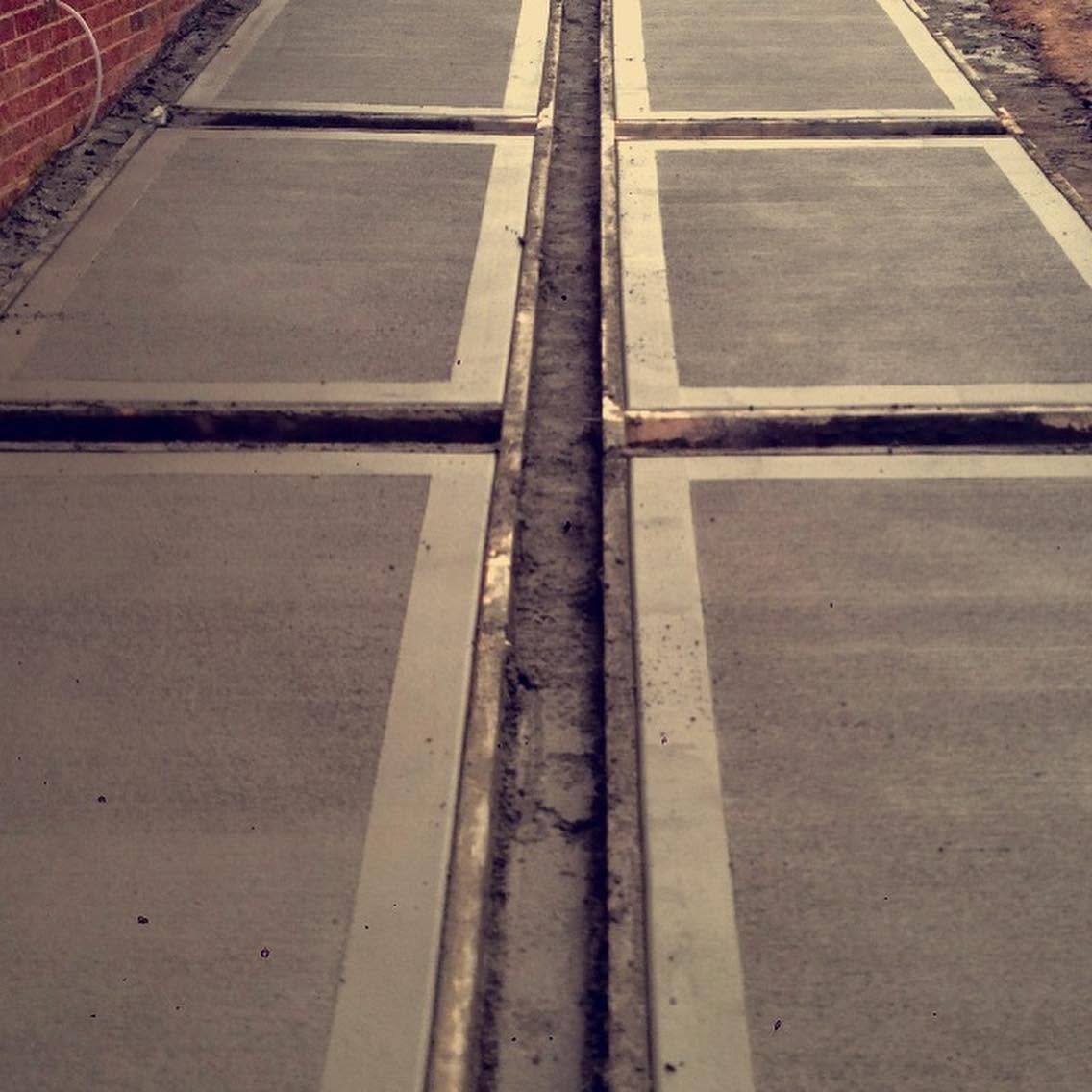 Concrete sidewalk slabs with a narrow central drainage channel, viewed from above