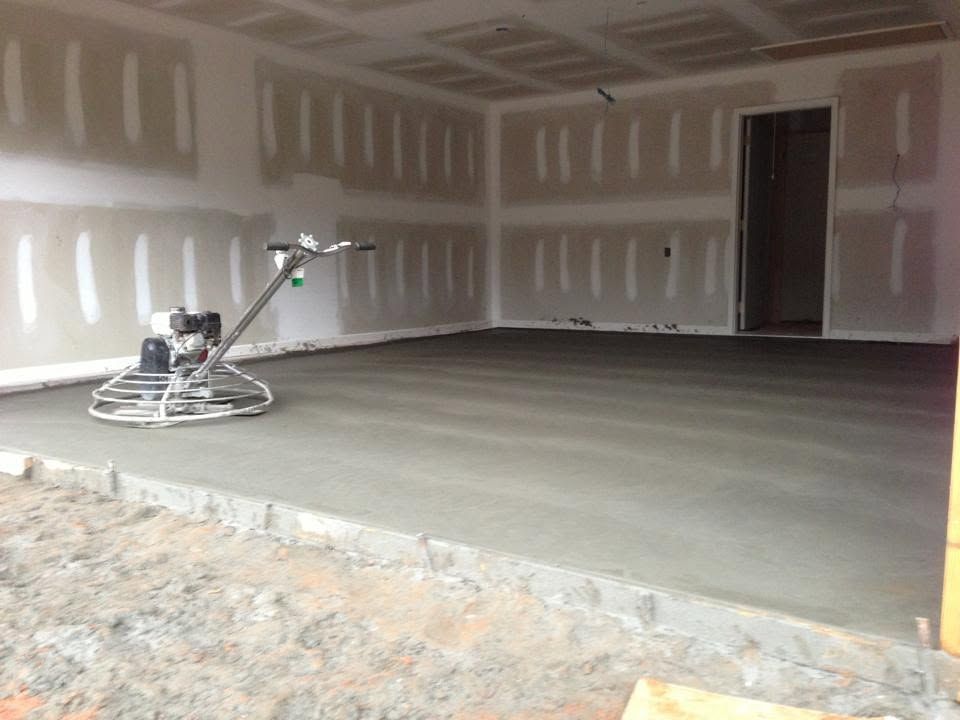 Interior of unfinished garage with drywall, concrete floor, and a floor grinder in use