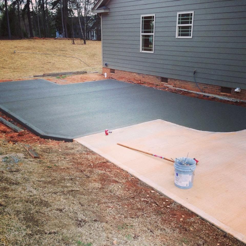Black paving laid beside a gray house, with a tan section and bucket in the foreground.