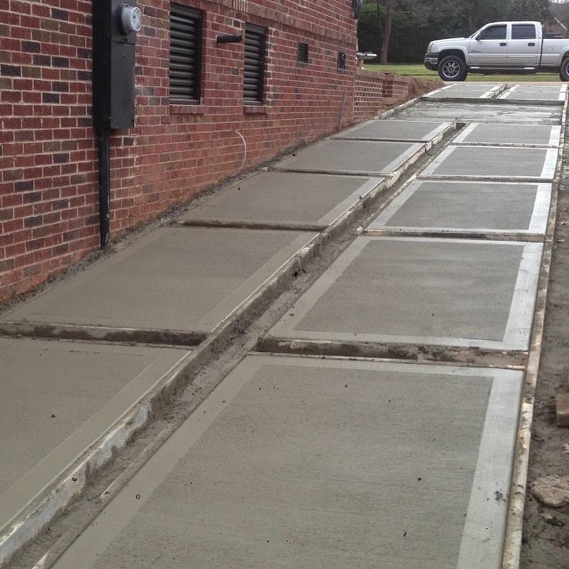 Concrete sidewalk ramps beside a brick building, showing uneven slabs and a parked pickup in the distance