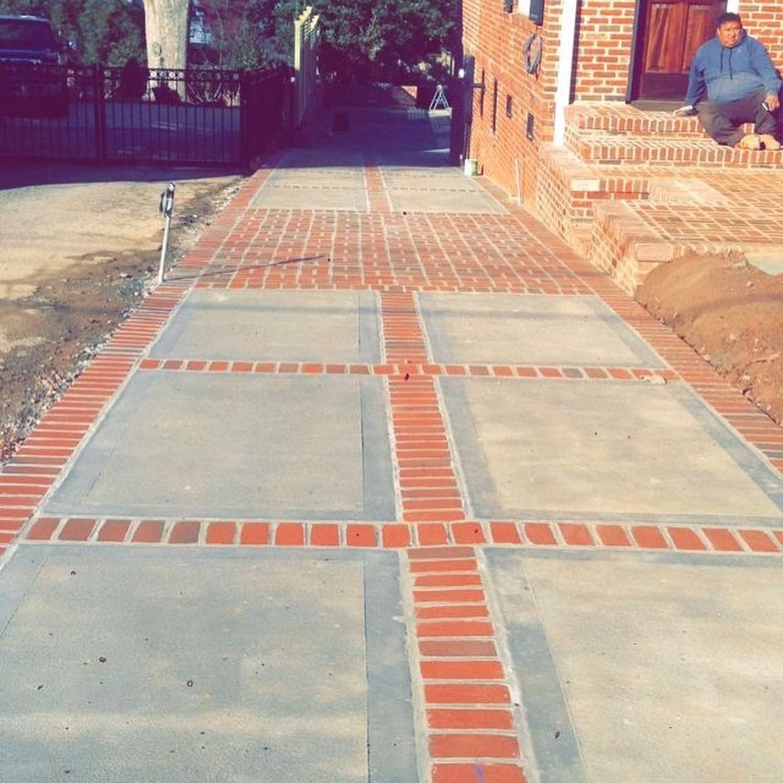 Brick-and-concrete sidewalk leading to a house entrance, with a person sitting on the porch in the background