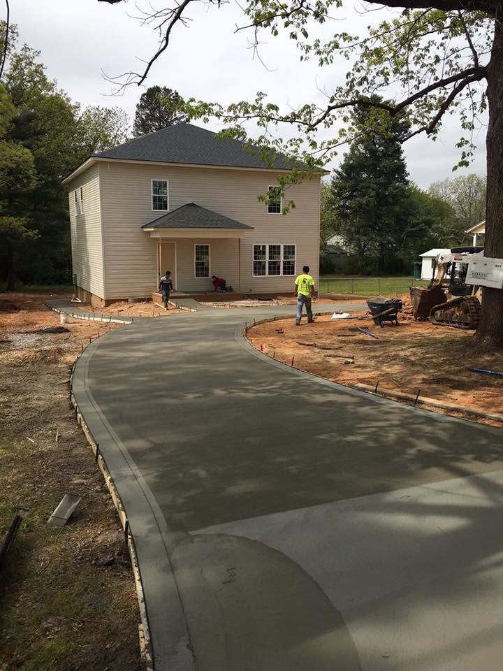 New concrete driveway leading to a beige house under construction, with a worker nearby.