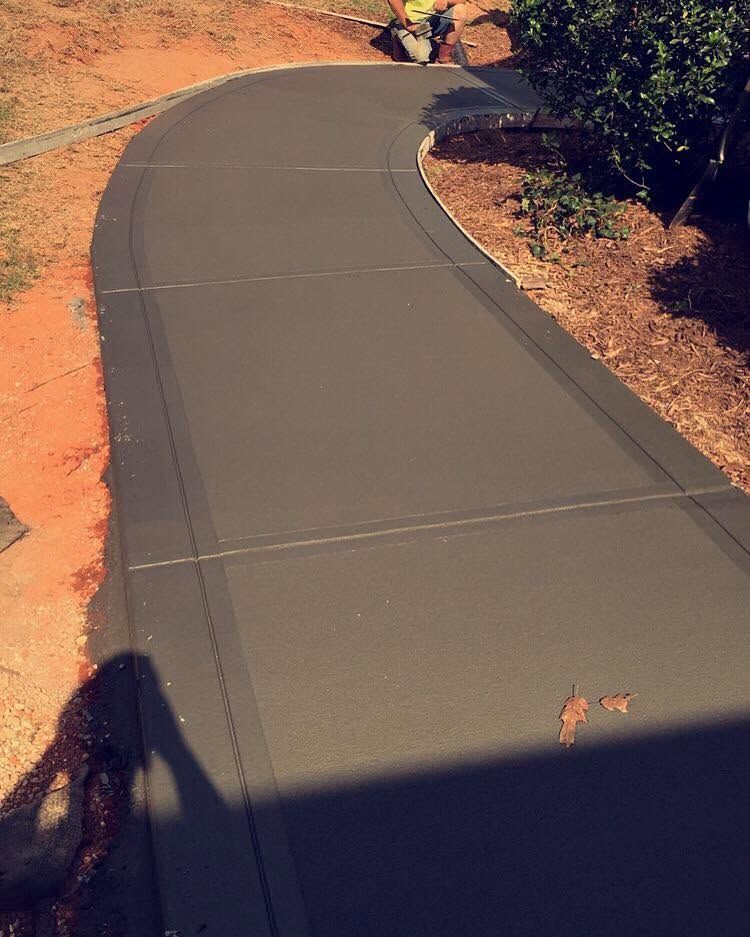 Curving paved path through dry, reddish terrain with trees casting shadows