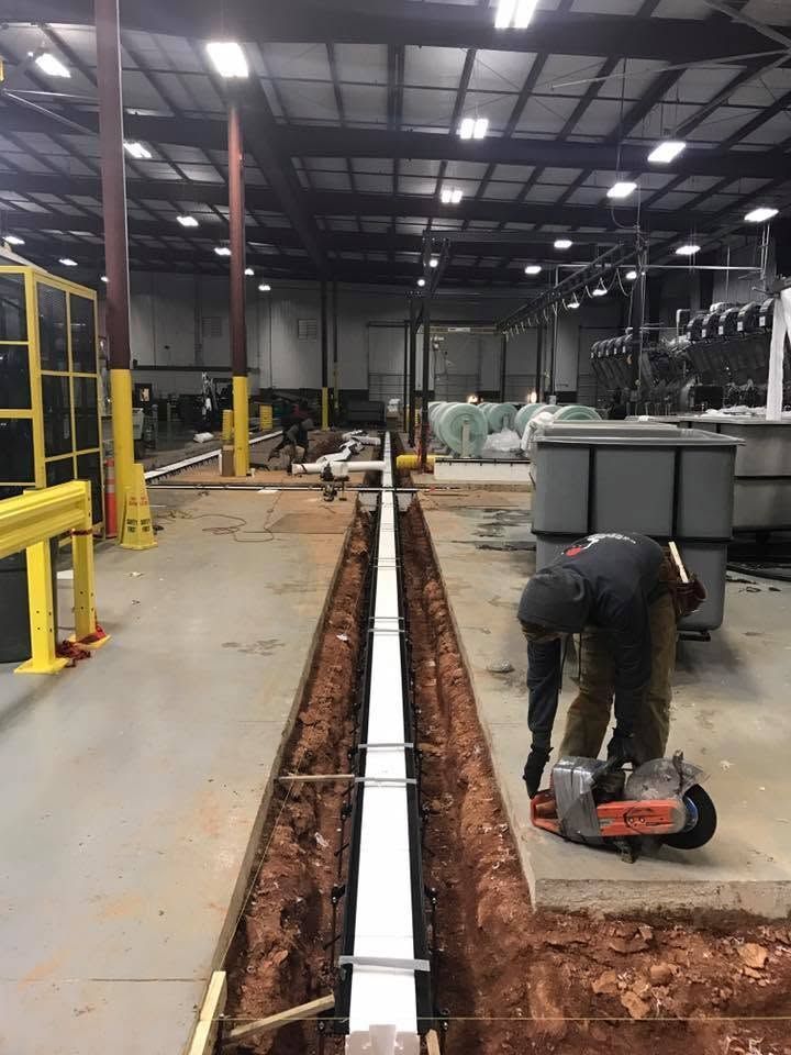 Worker cutting concrete beside a long trench in an industrial warehouse
