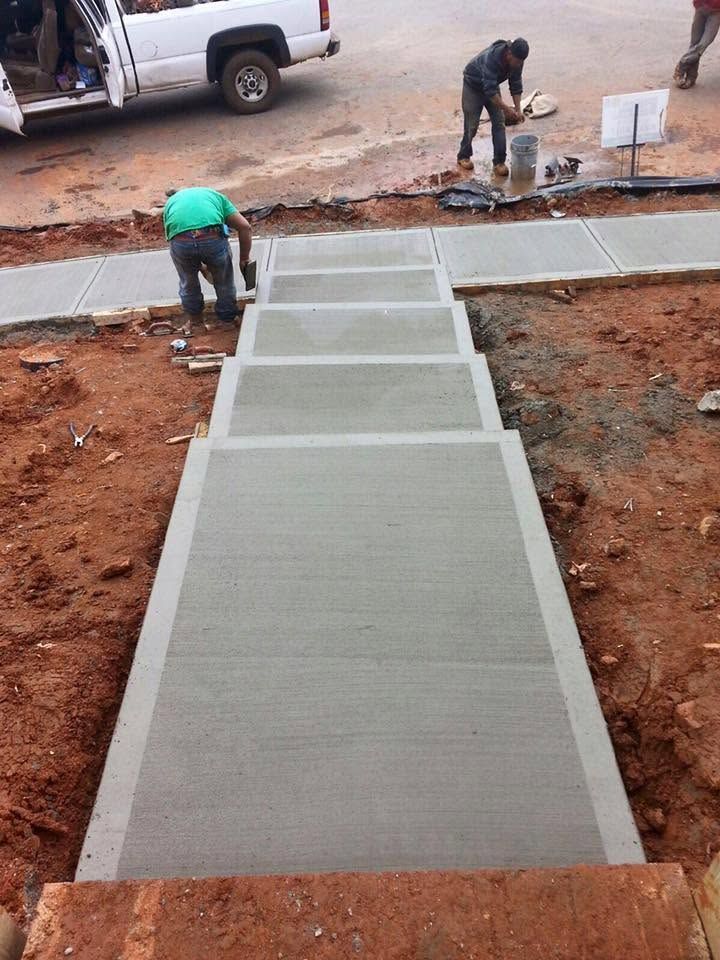 Workers smoothing a long concrete sidewalk ramp with steps at a roadside construction site