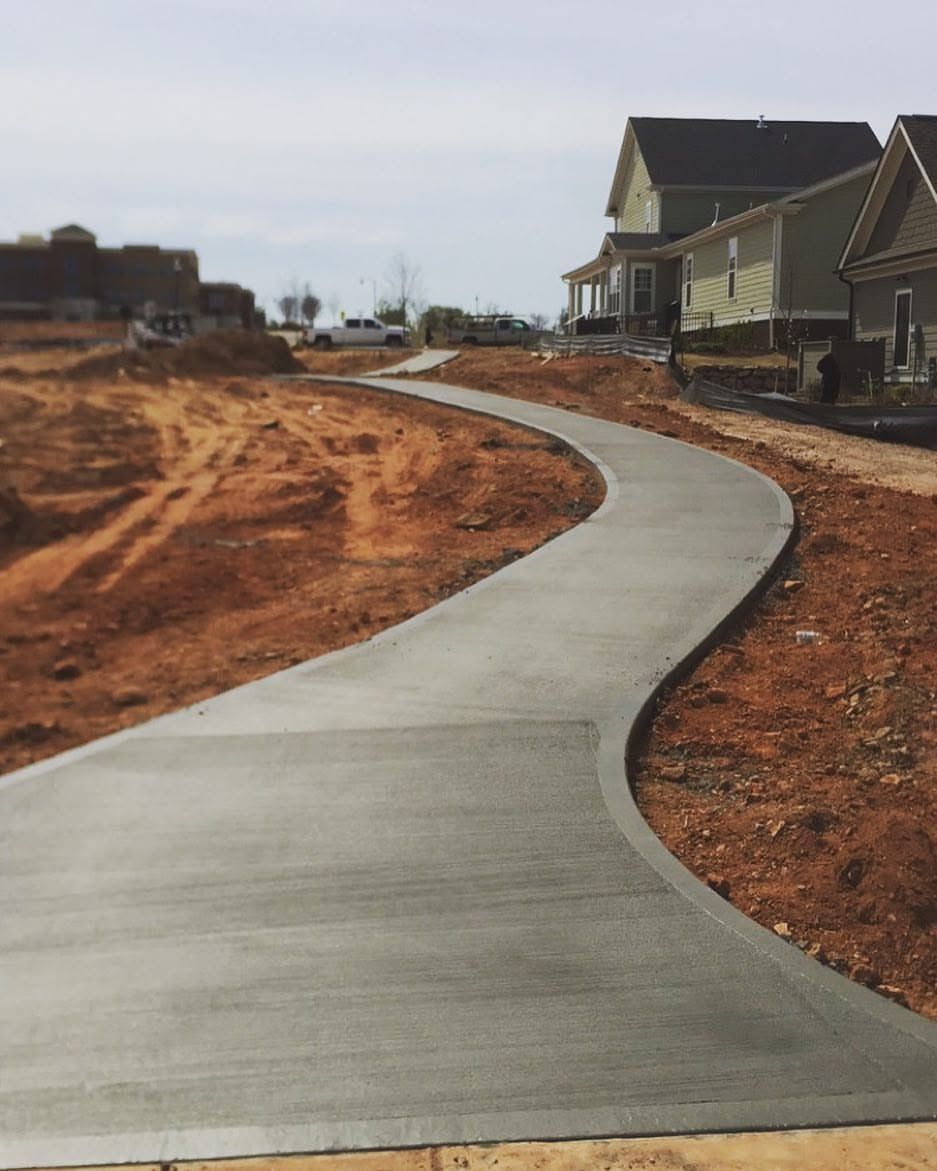 Curving concrete sidewalk through a newly built residential area with houses on the right and bare earth around it