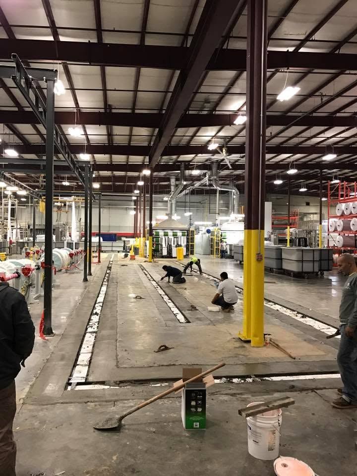 Warehouse interior with workers painting floor lines and columns under high industrial ceilings