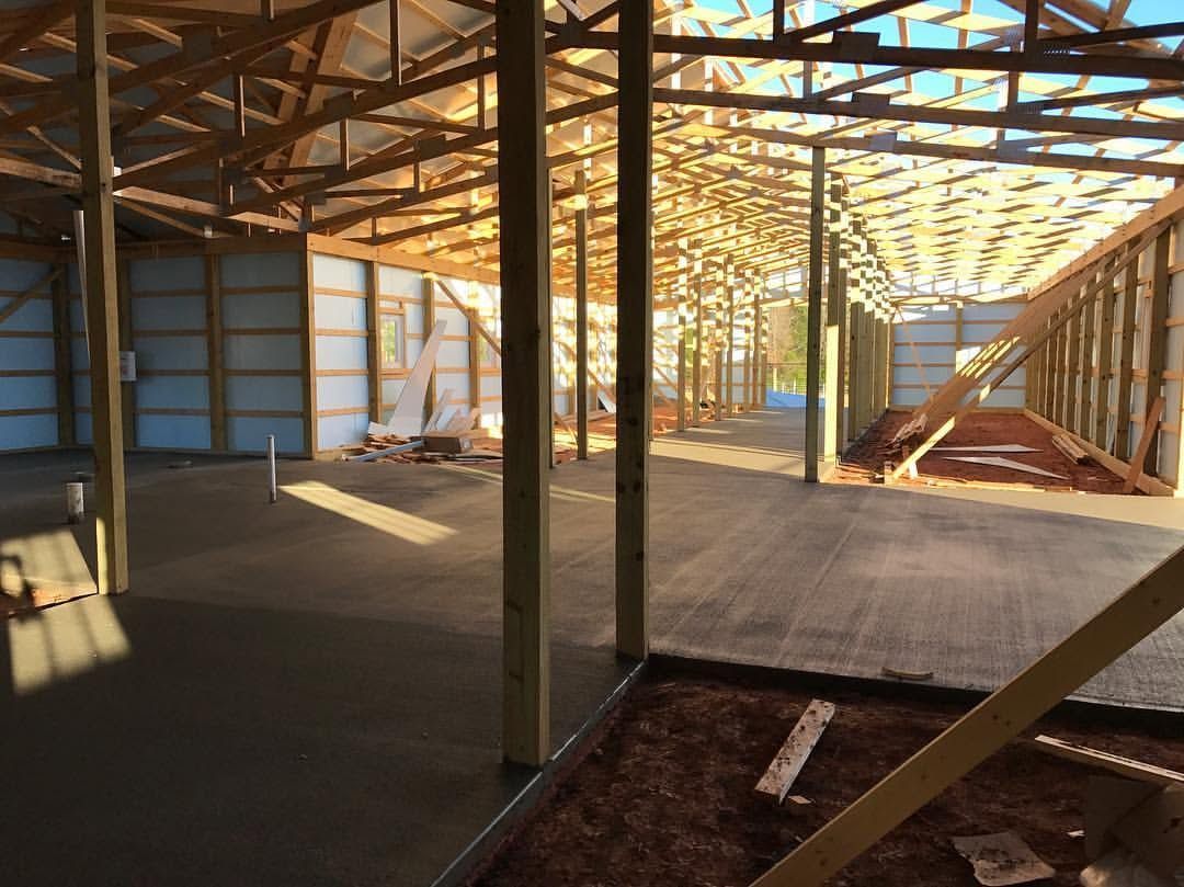 Interior of a partially built wooden structure with exposed beams and sunlight streaming in.