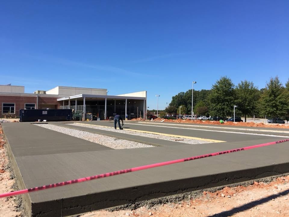 Construction site with a partially paved area, building, and two people under a bright blue sky
