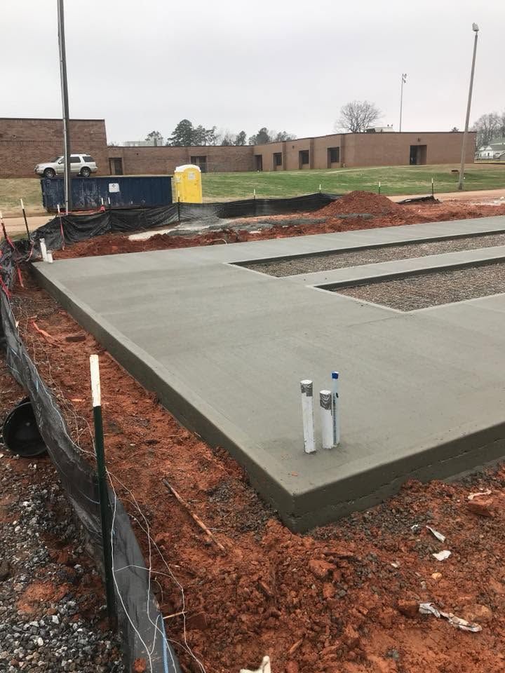 Fresh concrete slab at a construction site beside excavated red dirt and a fence