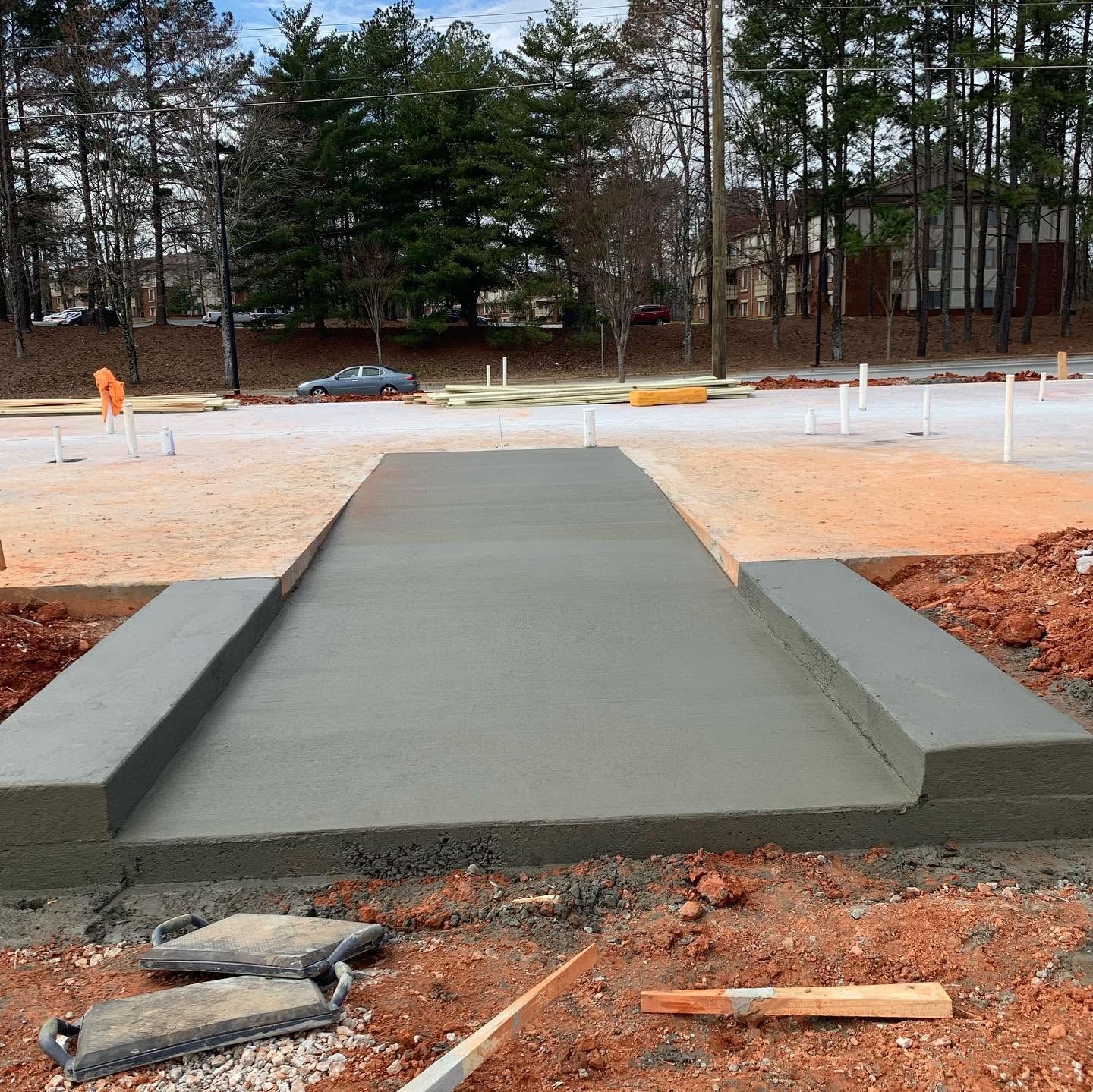 Fresh concrete walkway under construction in a sandy lot with trees in the background