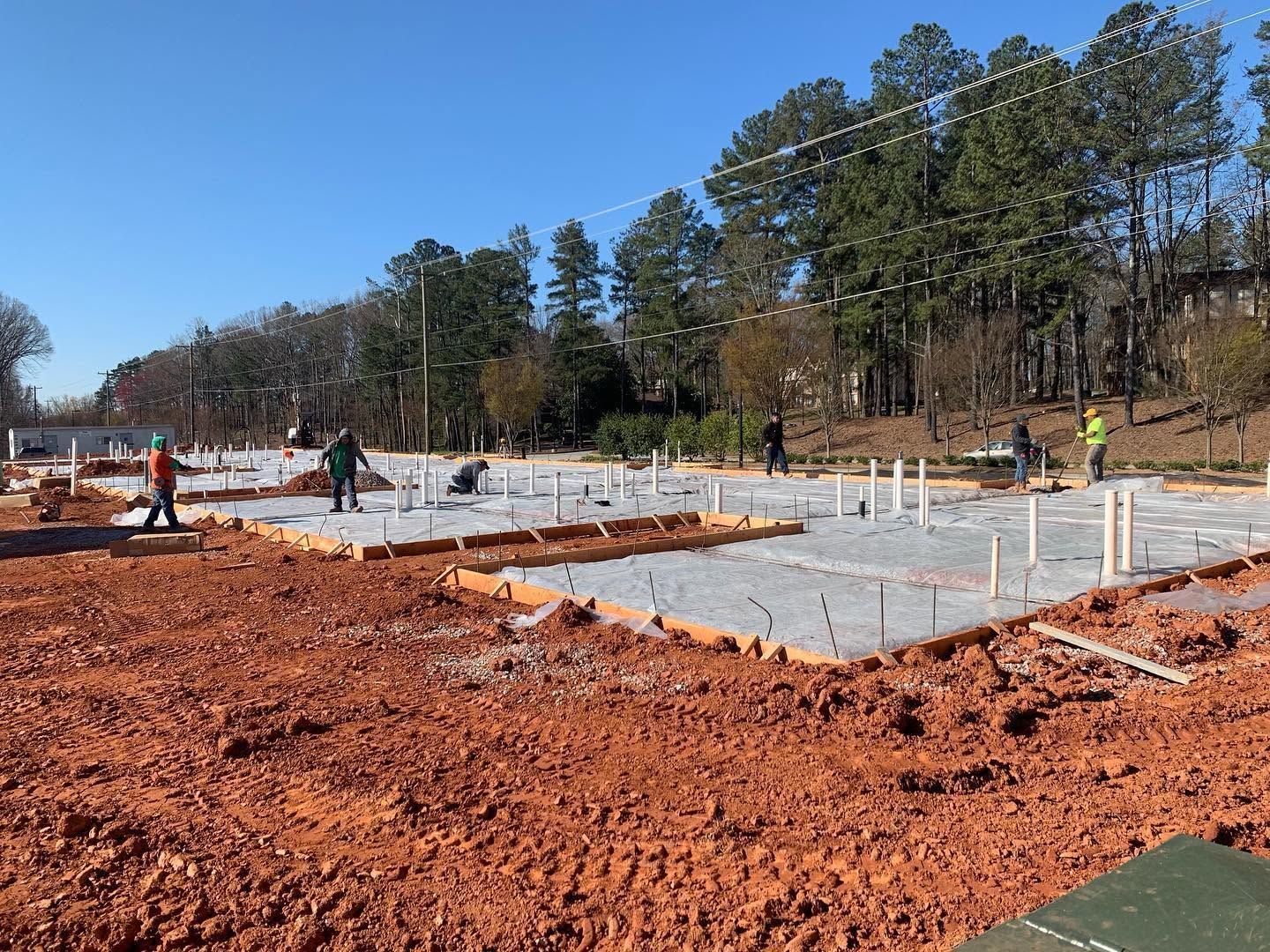 Construction site with concrete foundation slabs, workers, and orange dirt under a clear blue sky