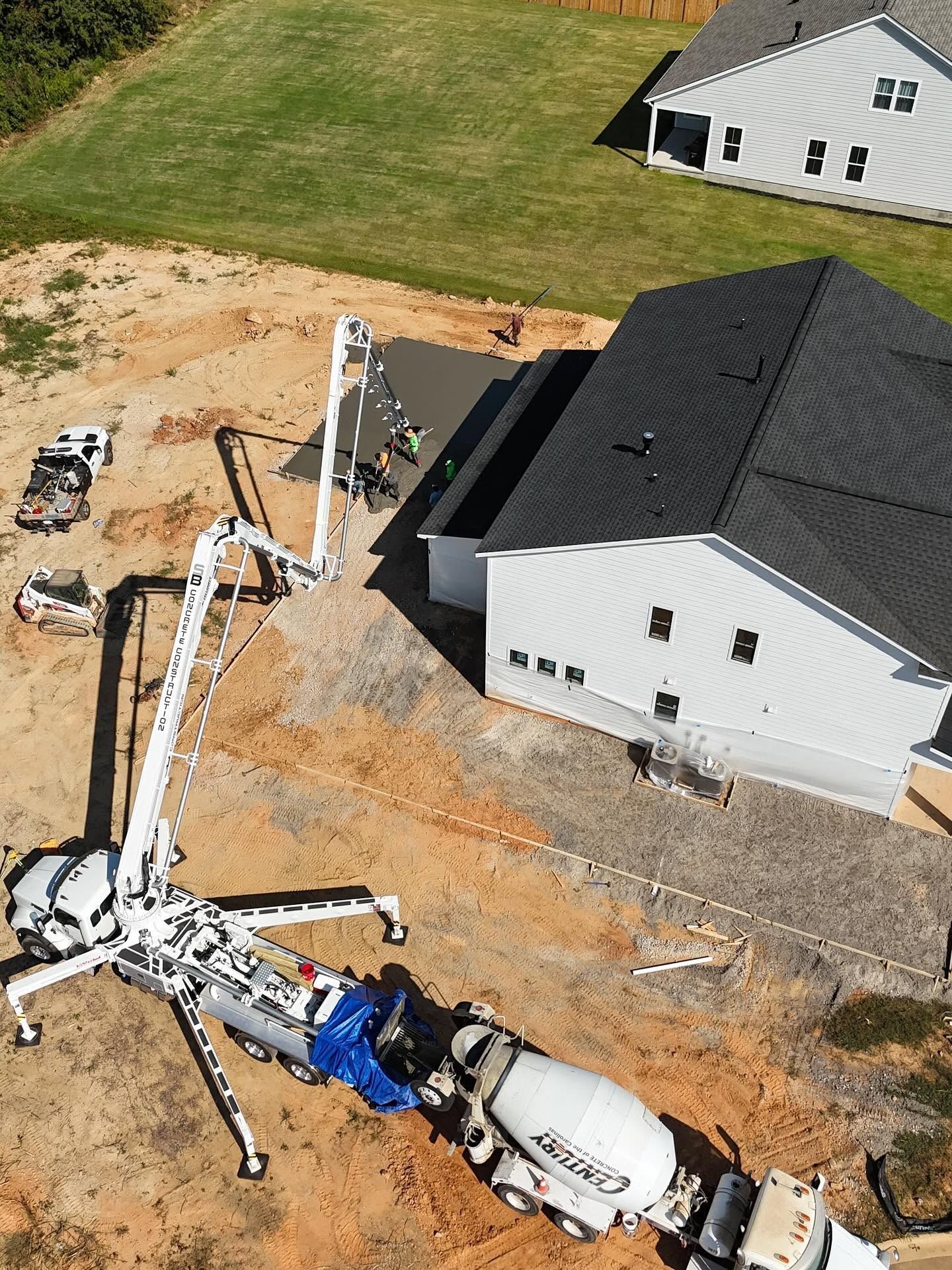 Aerial view of a concrete pump truck pouring near a white house under construction.