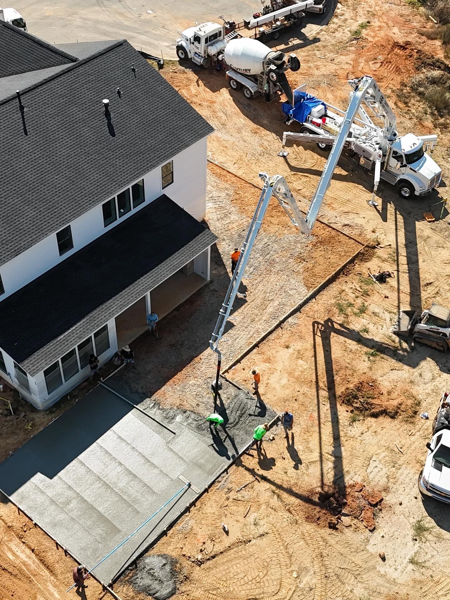 Aerial view of a house under construction with concrete trucks and workers on a dirt lot