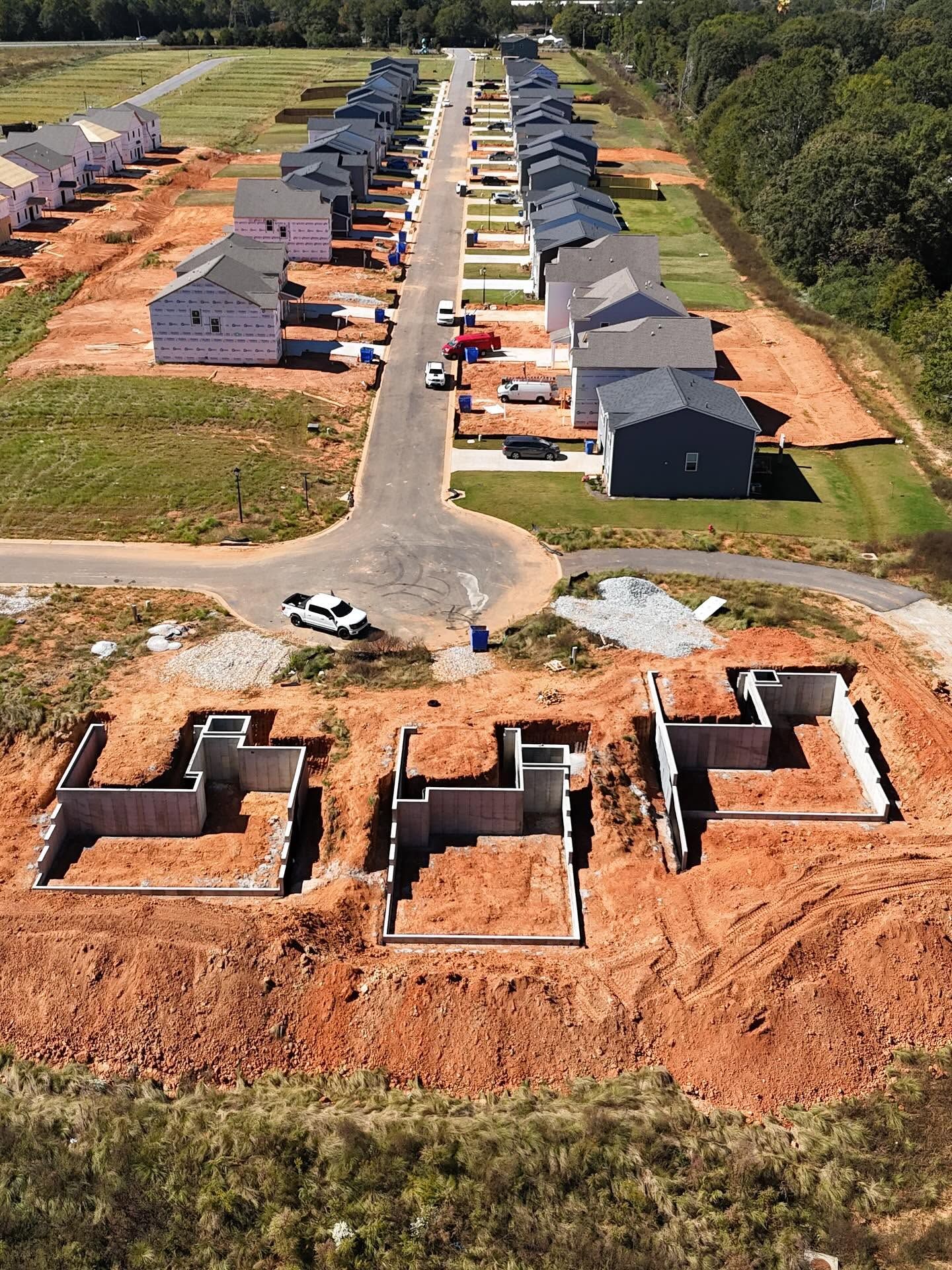 Aerial view of a new housing development with rows of houses and construction foundations in the foreground