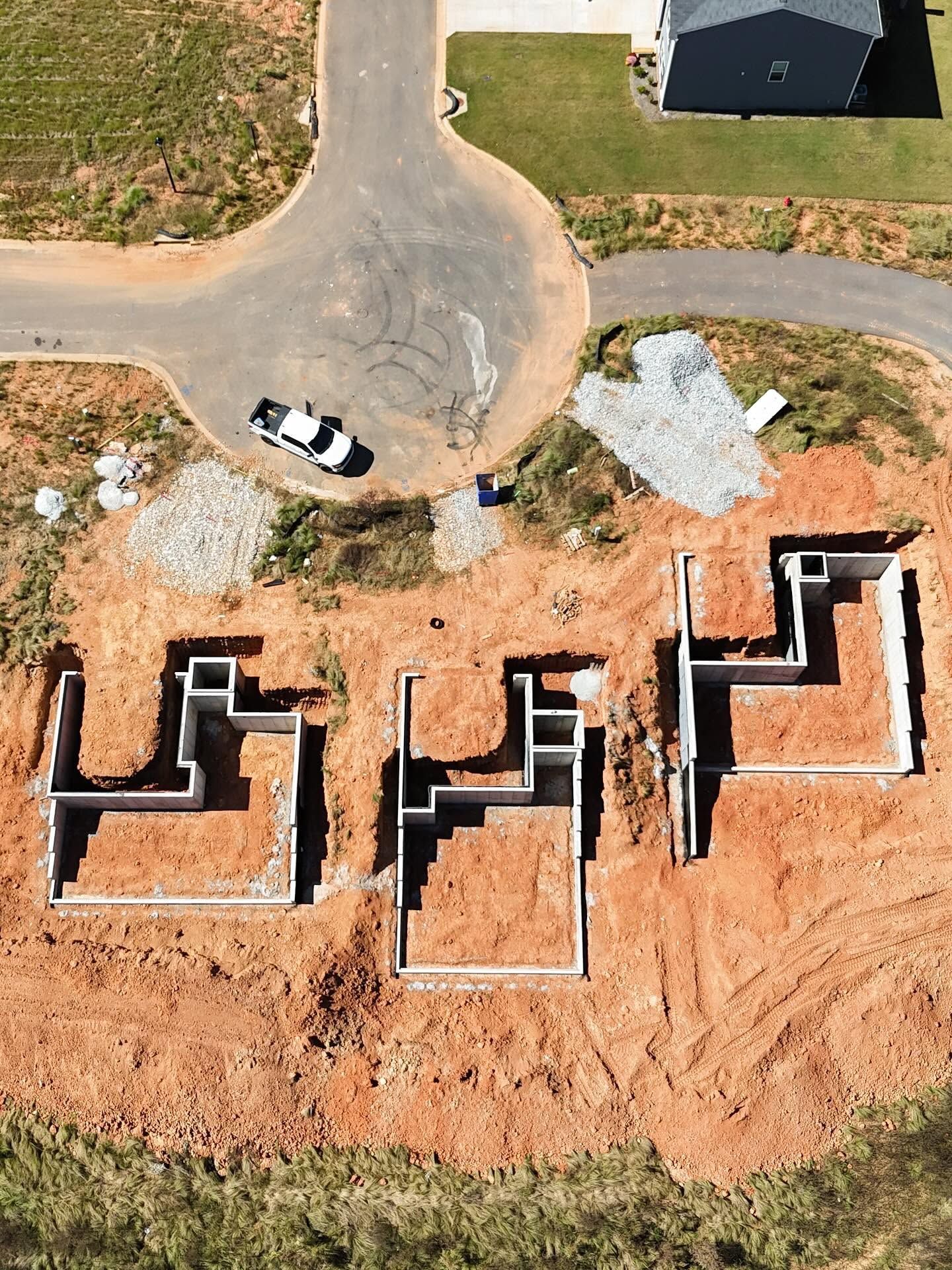 Aerial view of several brick foundation outlines on a construction site beside a curved road and parked pickup truck