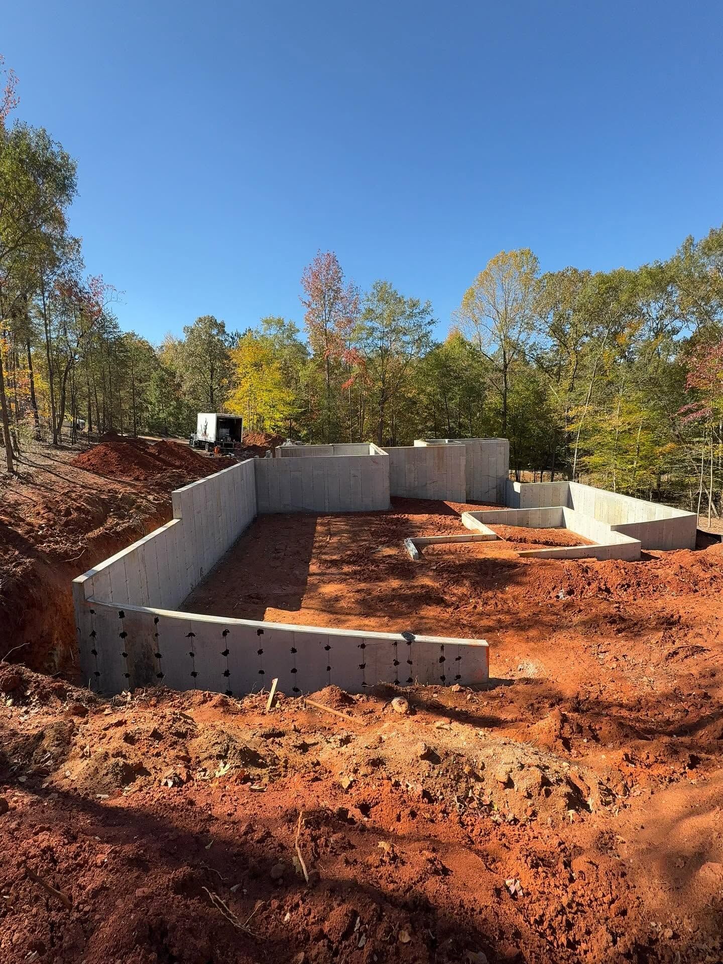 Concrete foundation walls under construction on a red dirt lot with trees and blue sky