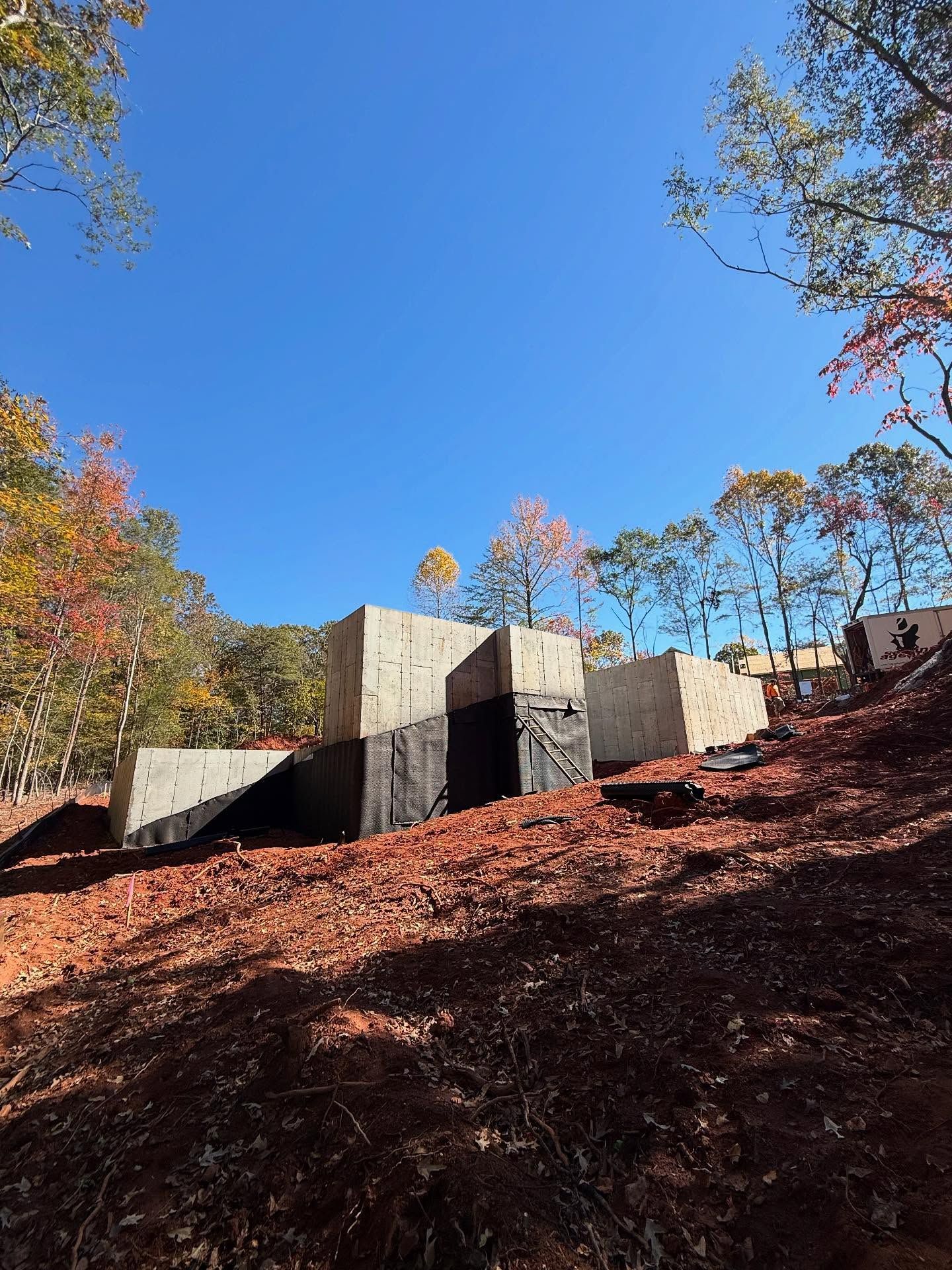 Concrete retaining wall on a wooded hillside under a clear blue sky in autumn.