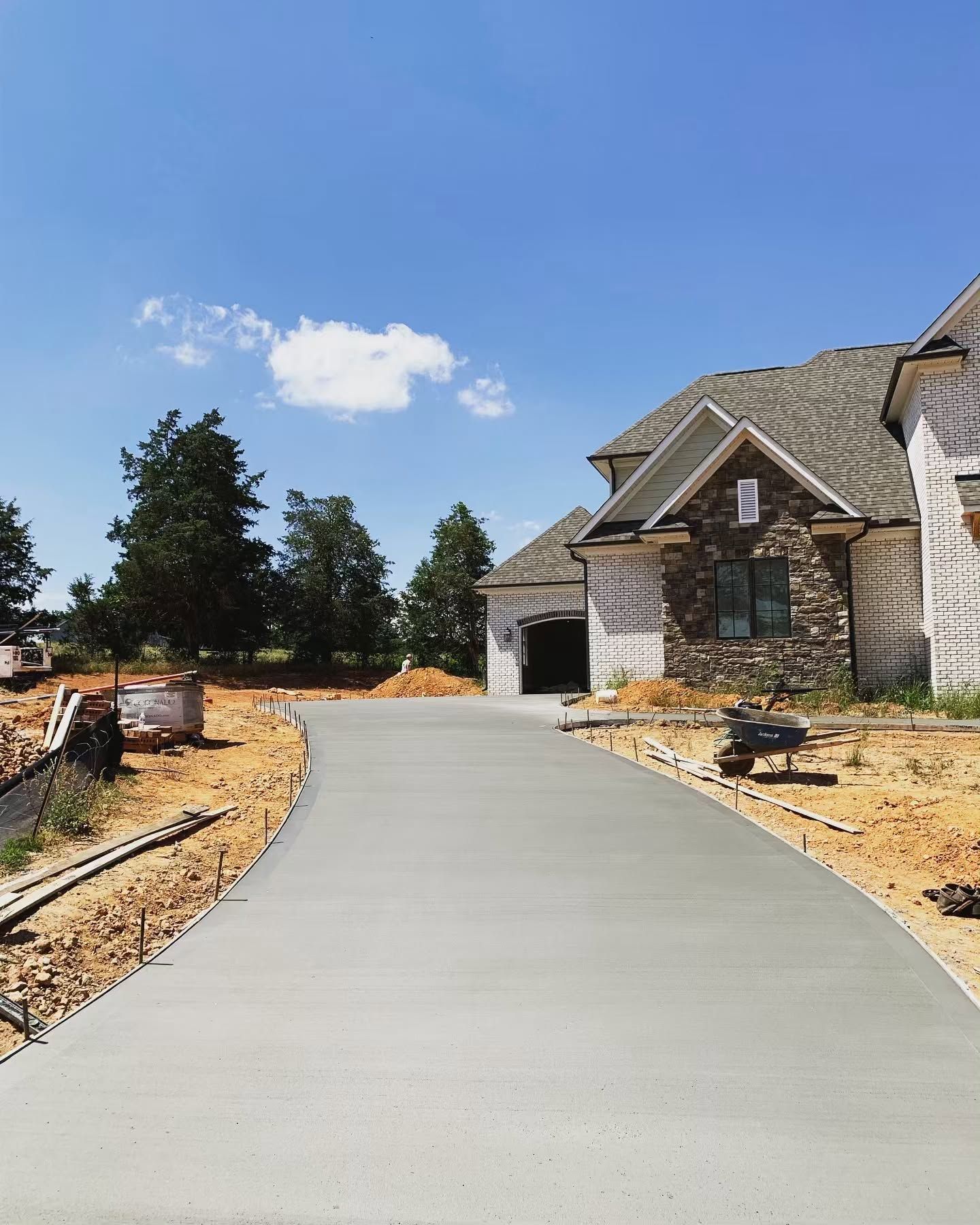 Curved concrete driveway leading to a stone house under a clear blue sky