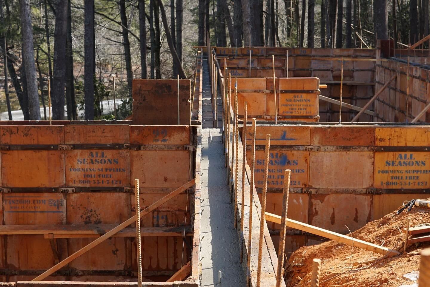 Orange concrete formwork at a construction site with a narrow central trench and forest in the background